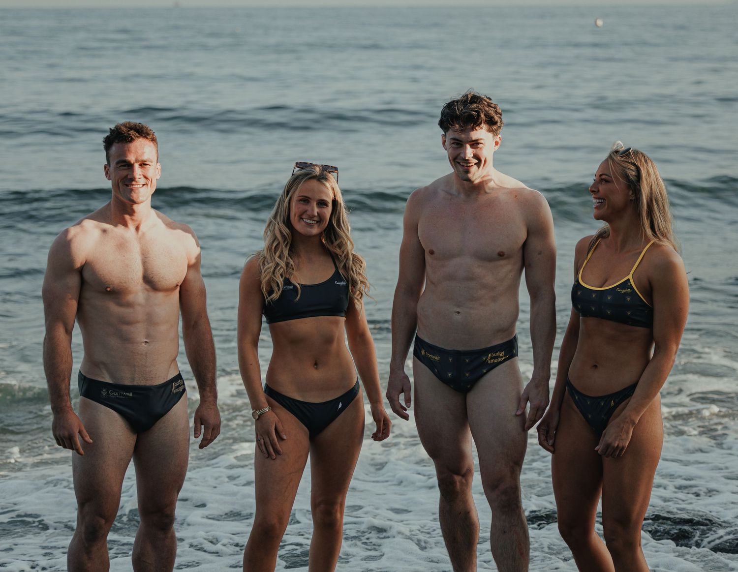 Group of friends in swimwear standing together at the beach during sunset.
