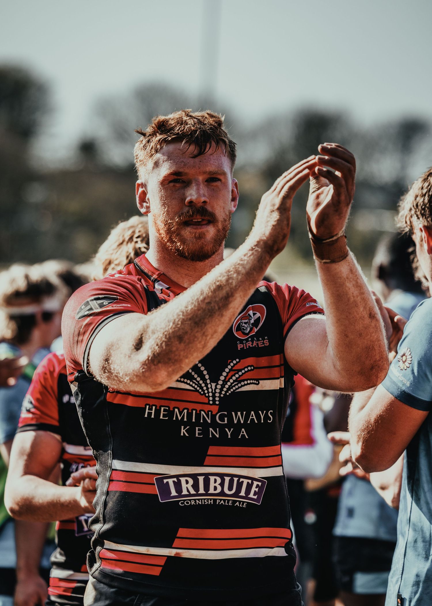 Rugby player in red striped jersey with sponsors clapping after game.