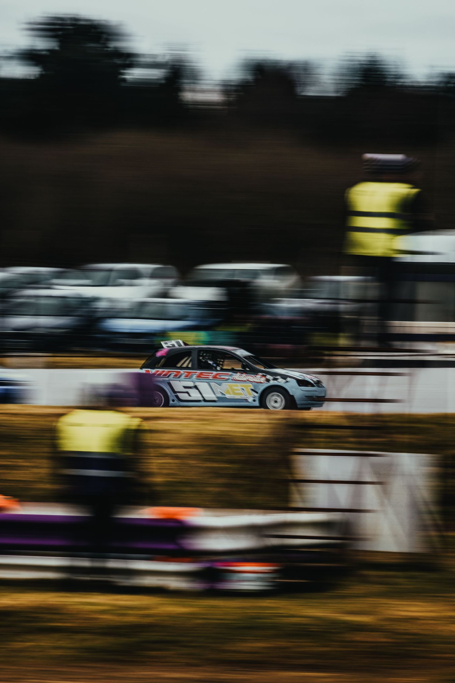 Race car speeding past yellow-clad spectators on track with motion blur effect.