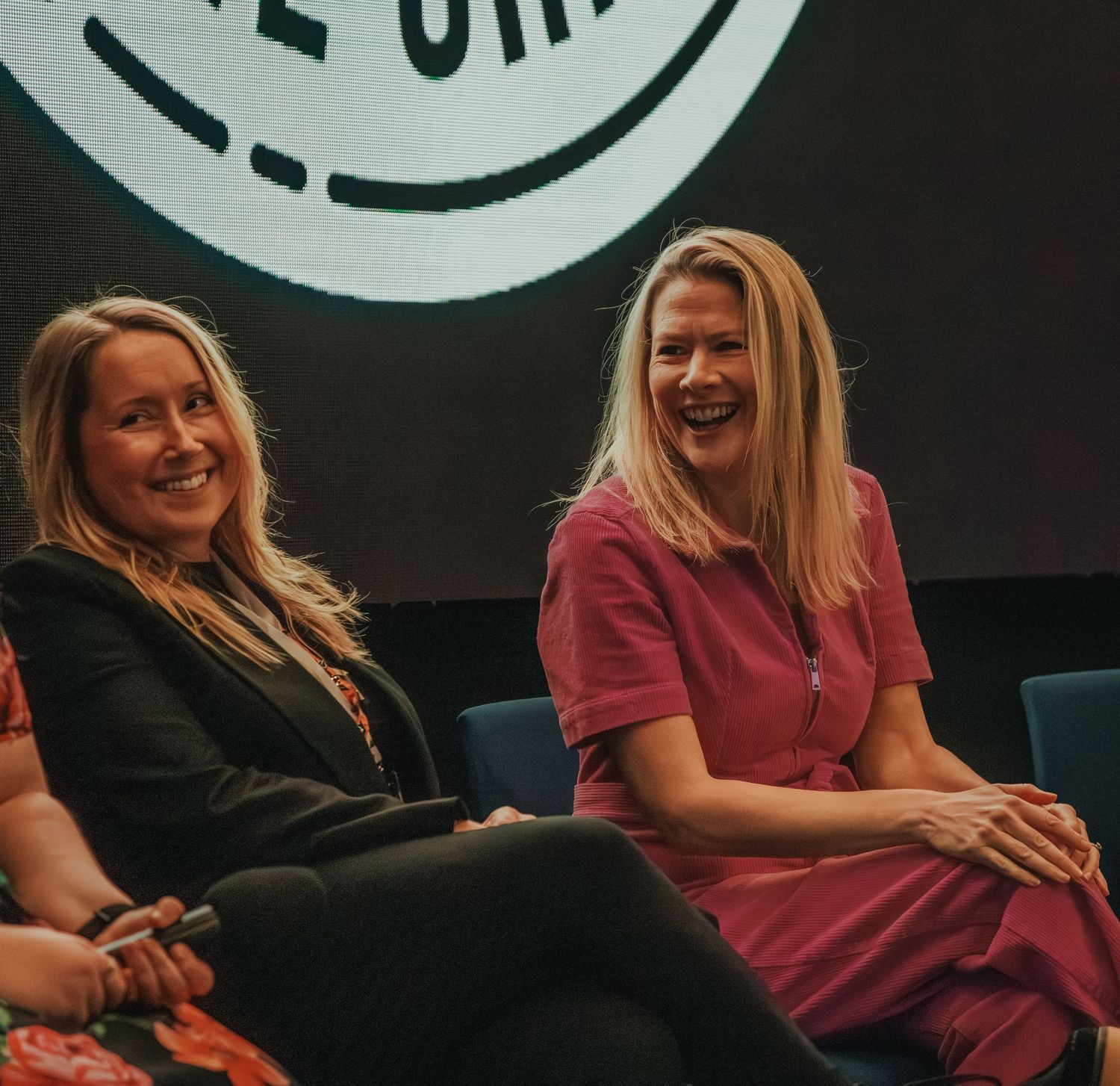 Two people sharing a laugh while sitting on chairs during an event.
