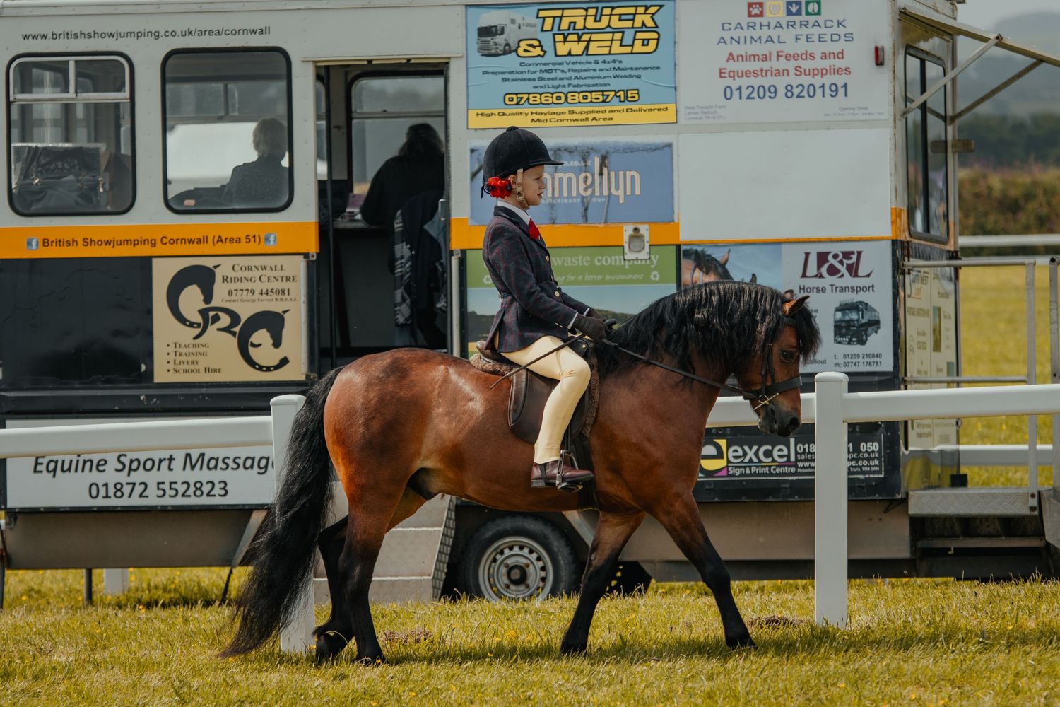 A brown horse and rider perform near a mobile concession stand at an outdoor equestrian event.