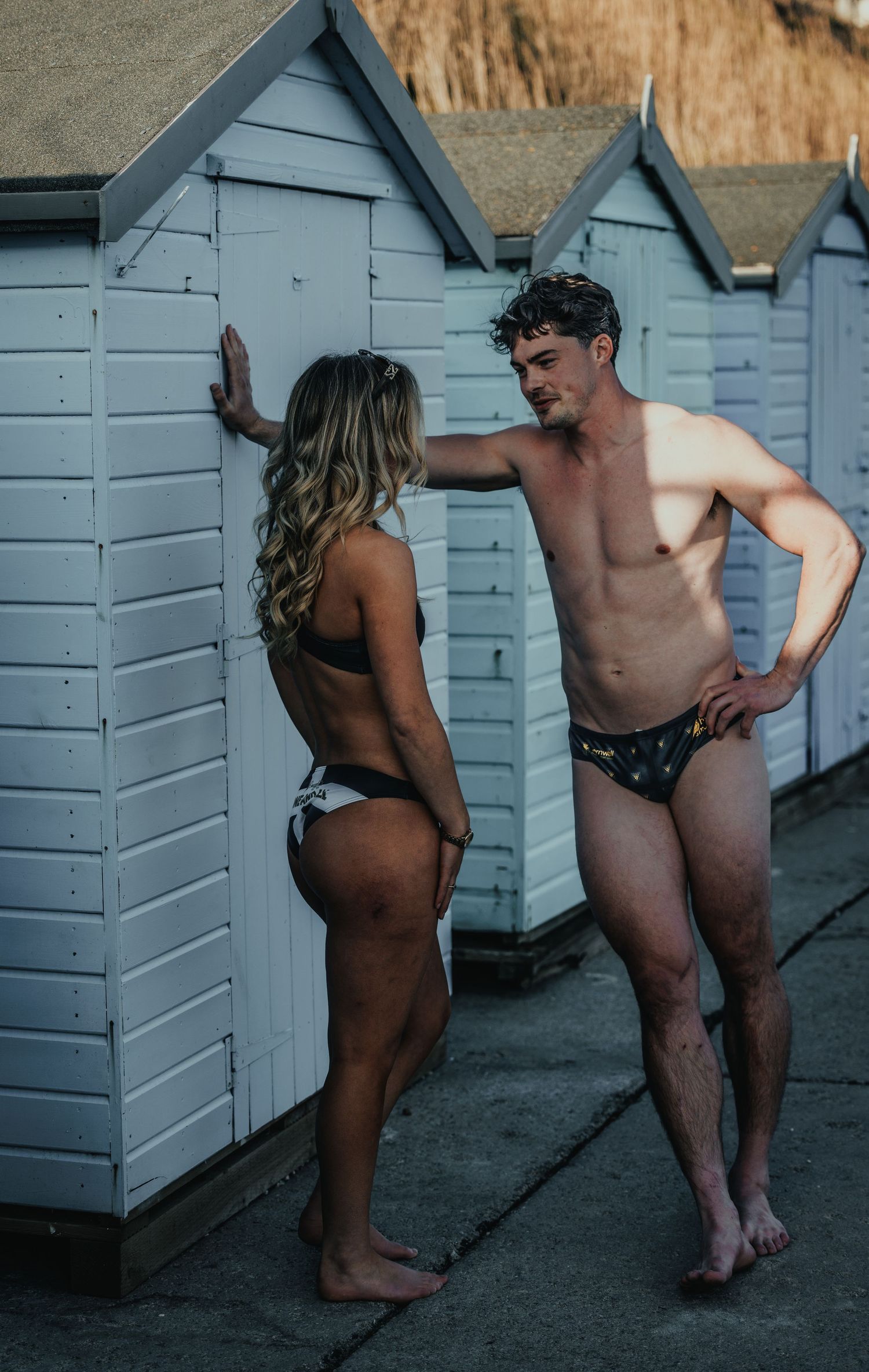 Two people in swimwear having conversation near row of beach huts.