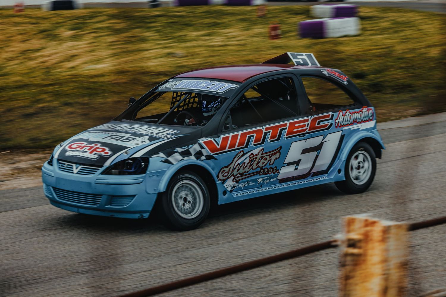Light blue race car number 51 speeds along track with custom racing livery and sponsor decals.