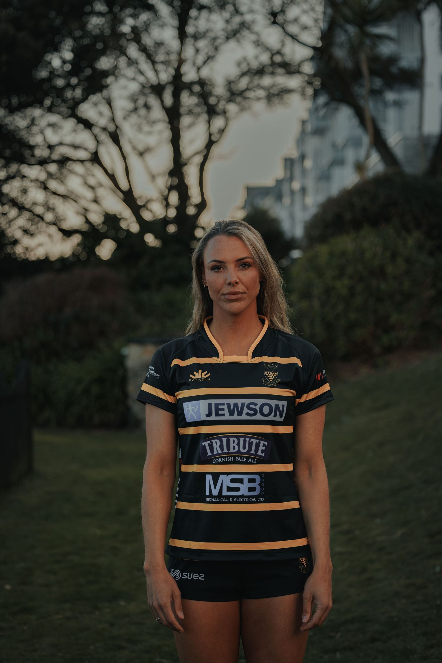 Person wearing black and yellow striped Jewson rugby jersey poses outdoors.