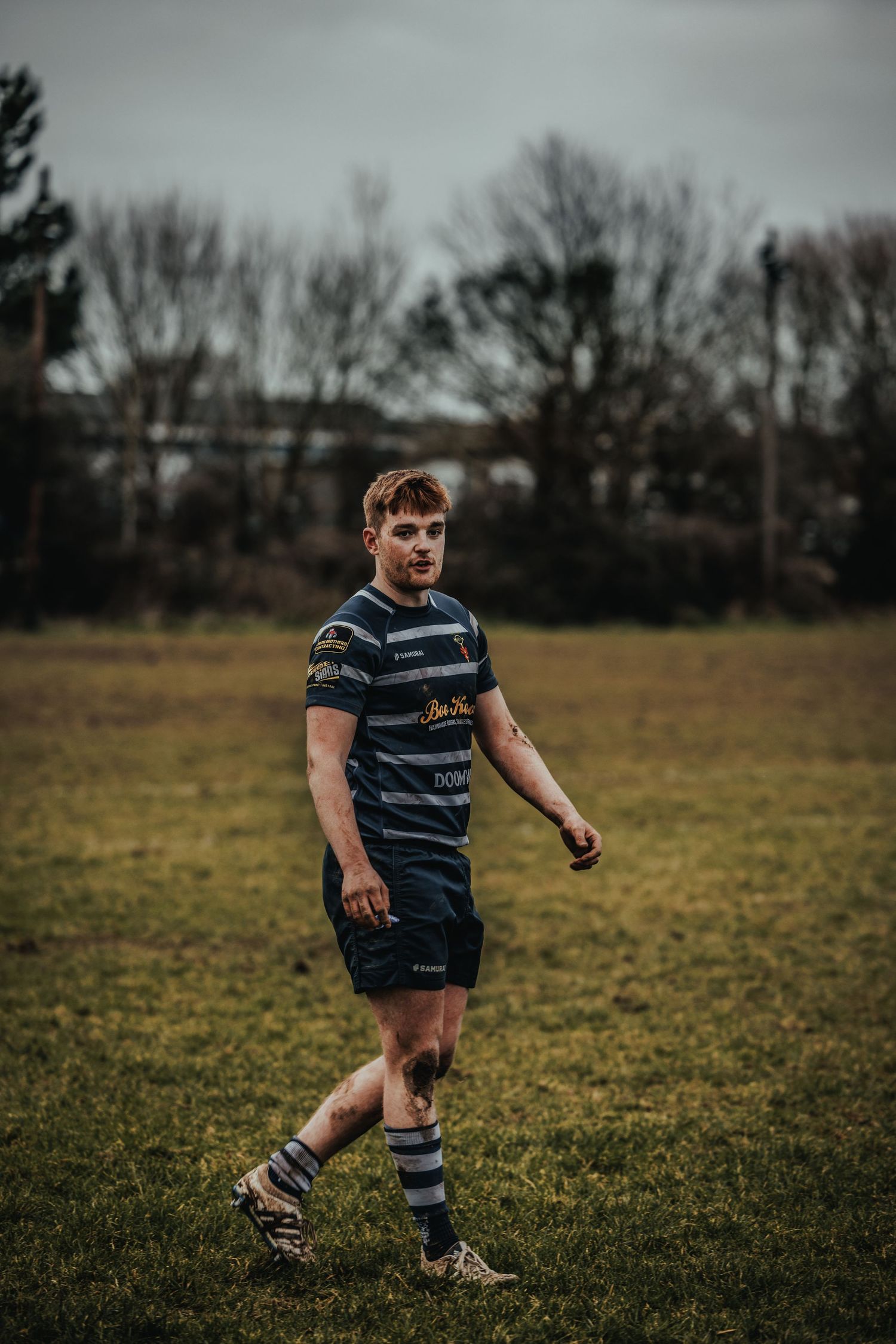 Rugby player in striped jersey walking across field during practice.