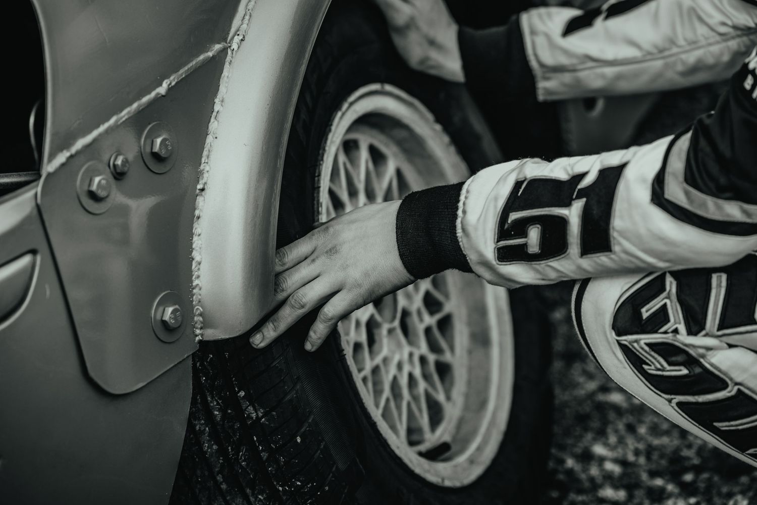 Black and white detail of racing glove touching car wheel during motorsport event.