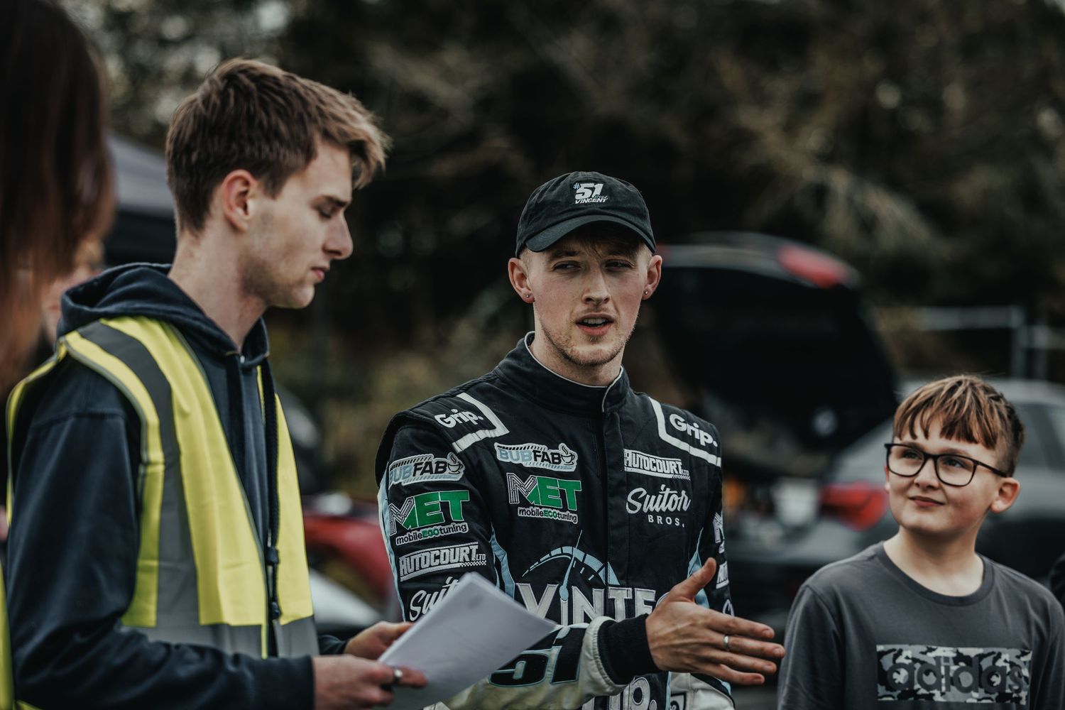 Racing driver in Vintec gear discusses with team members at motorsport event.