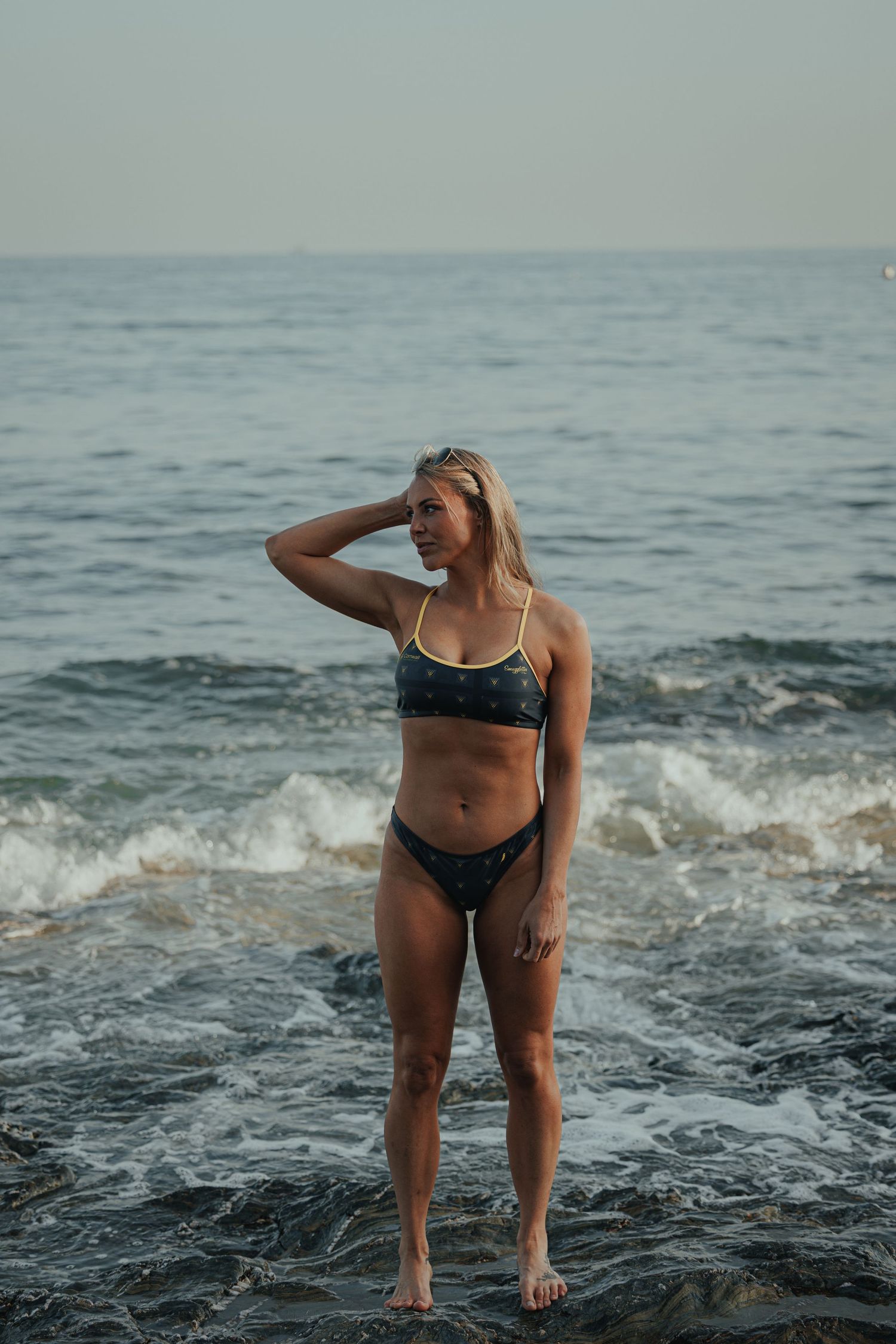 Athletic person in swimwear stands confidently in ocean waves at dusk.