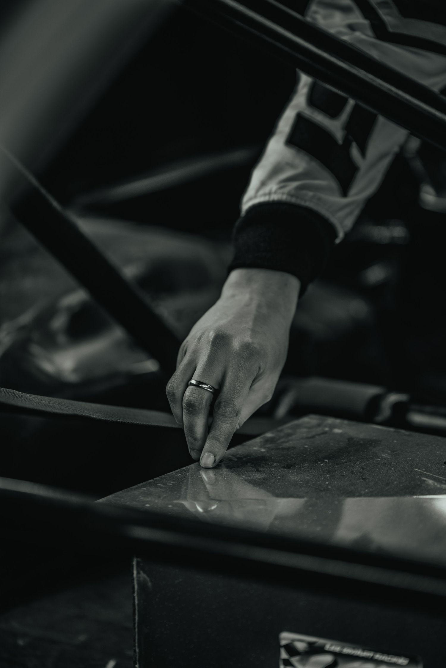 Close-up of gloved hand touching surface of racing vehicle in black and white.