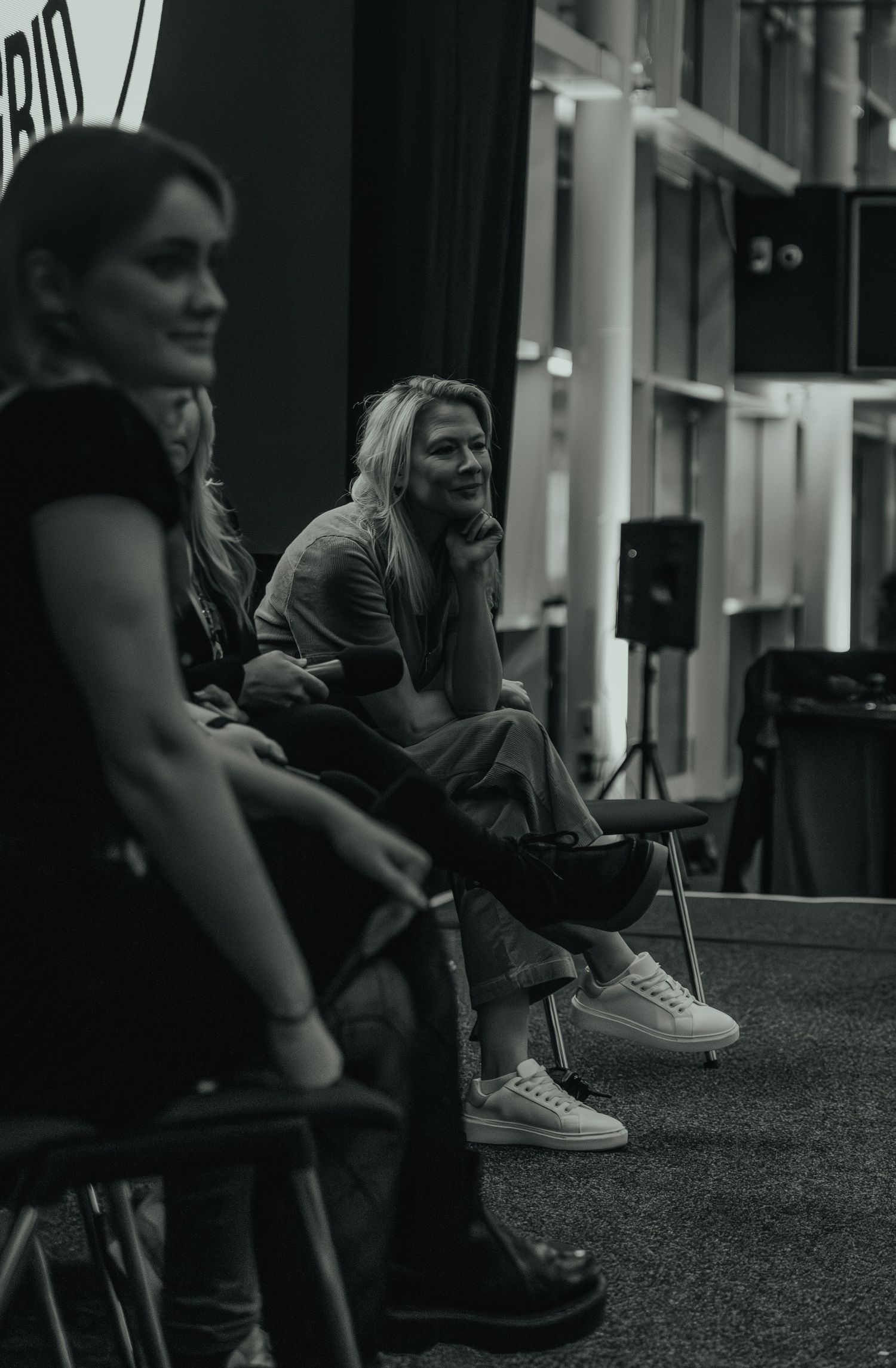 Two people sit casually in a dark studio space with black and white lighting.