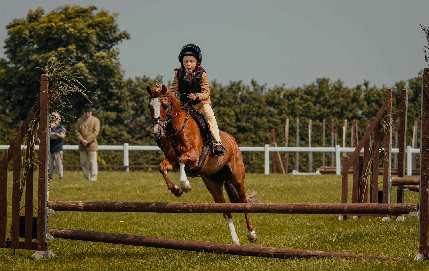 Equestrian and horse clearing a show jumping obstacle in front of white fencing during competition.