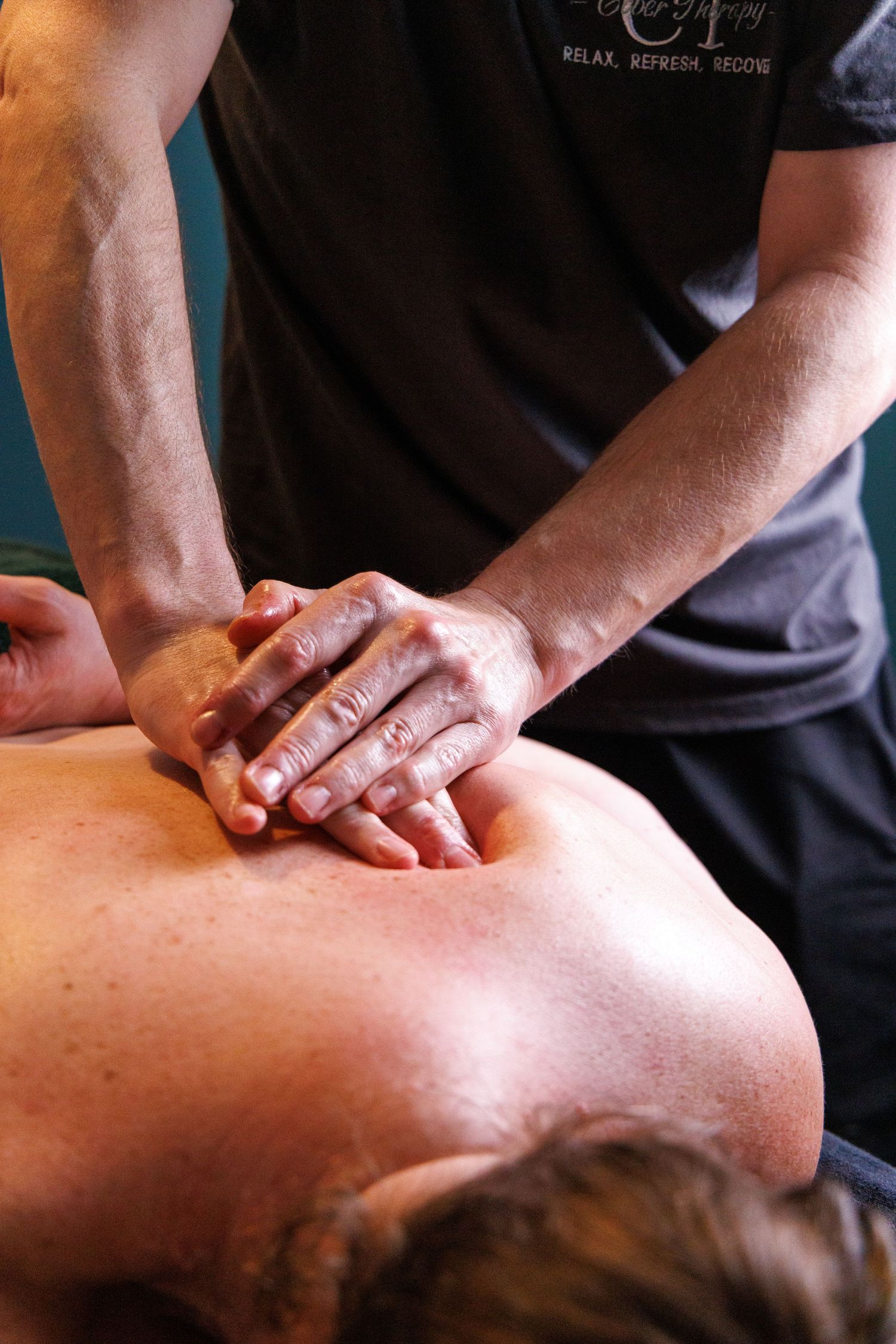A massage therapist performing deep tissue back massage on a client lying on a massage table.