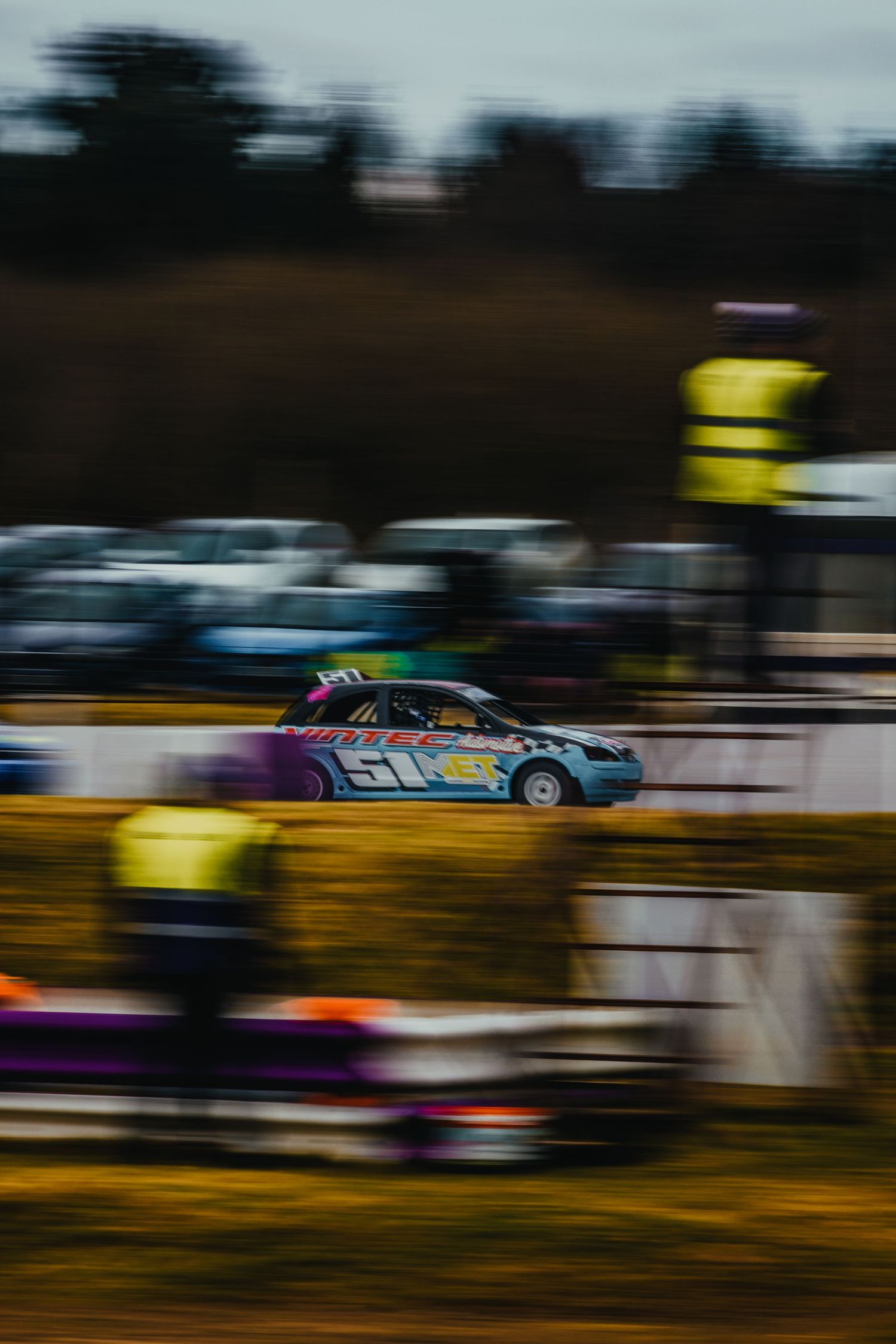 Racing car in action on track with blurred motion and spectators in background.