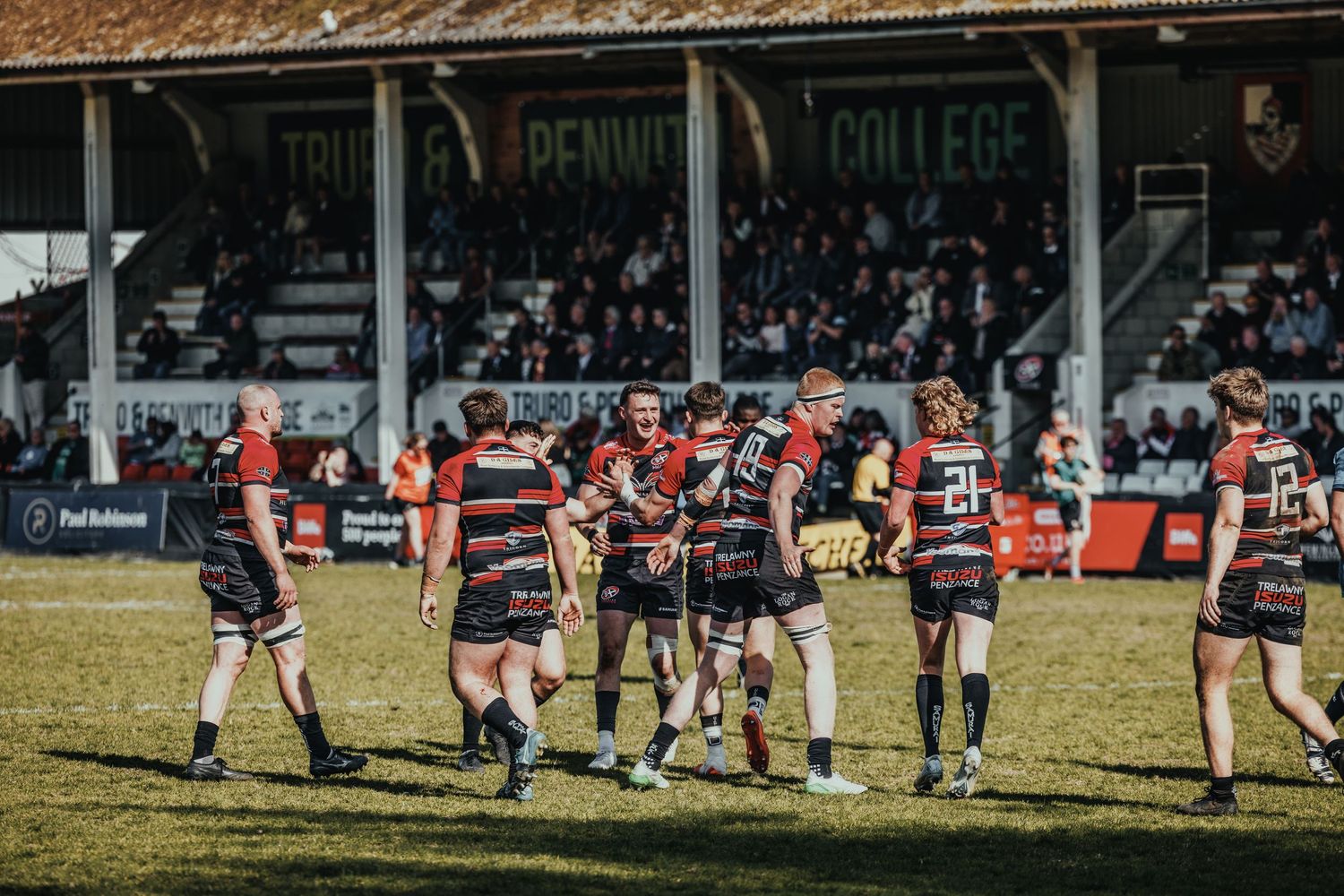 Rugby teams competing on field with crowded stadium grandstand in background.