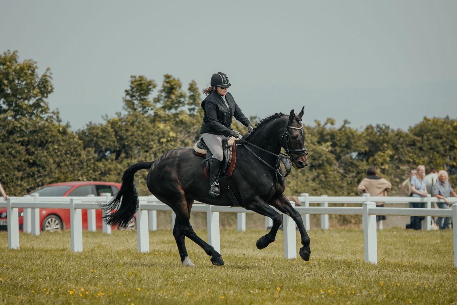Equestrian rider competing on black horse in dressage event at outdoor arena with white fencing.