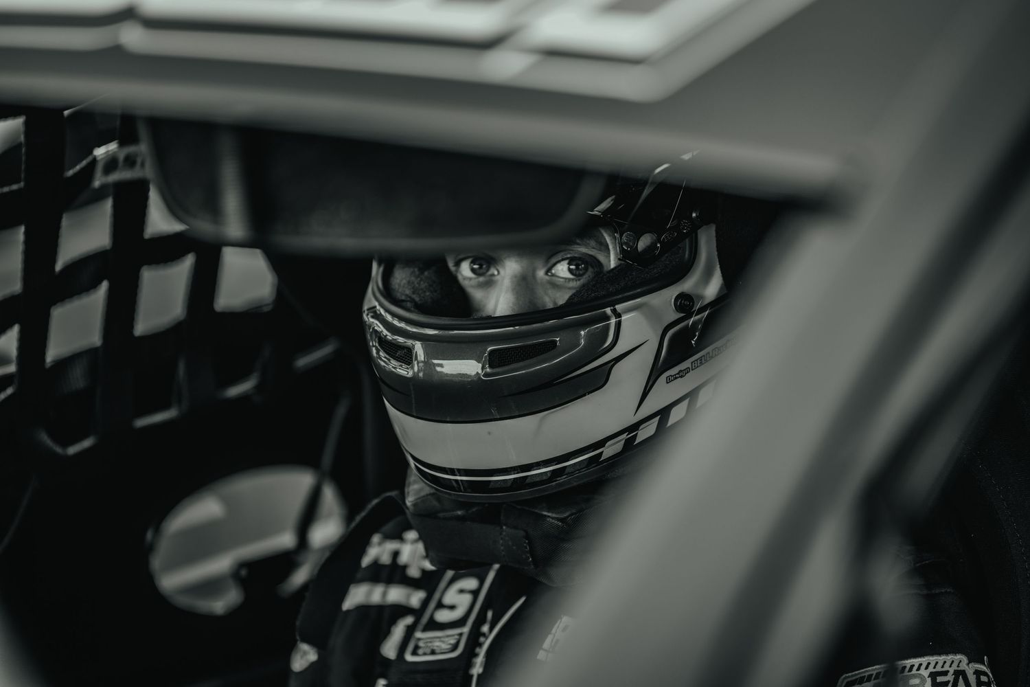 Black and white view of racing helmet through protective netting inside race car.