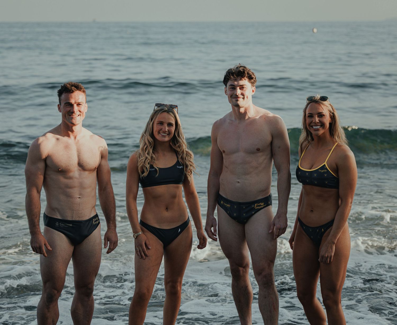 Group of friends posing together in swimwear at beach during sunset.