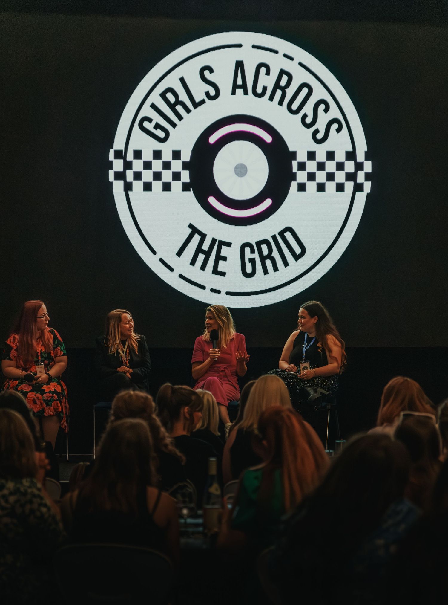 Panel discussion event with 'Girls Across The Grid' logo and audience in dark room.
