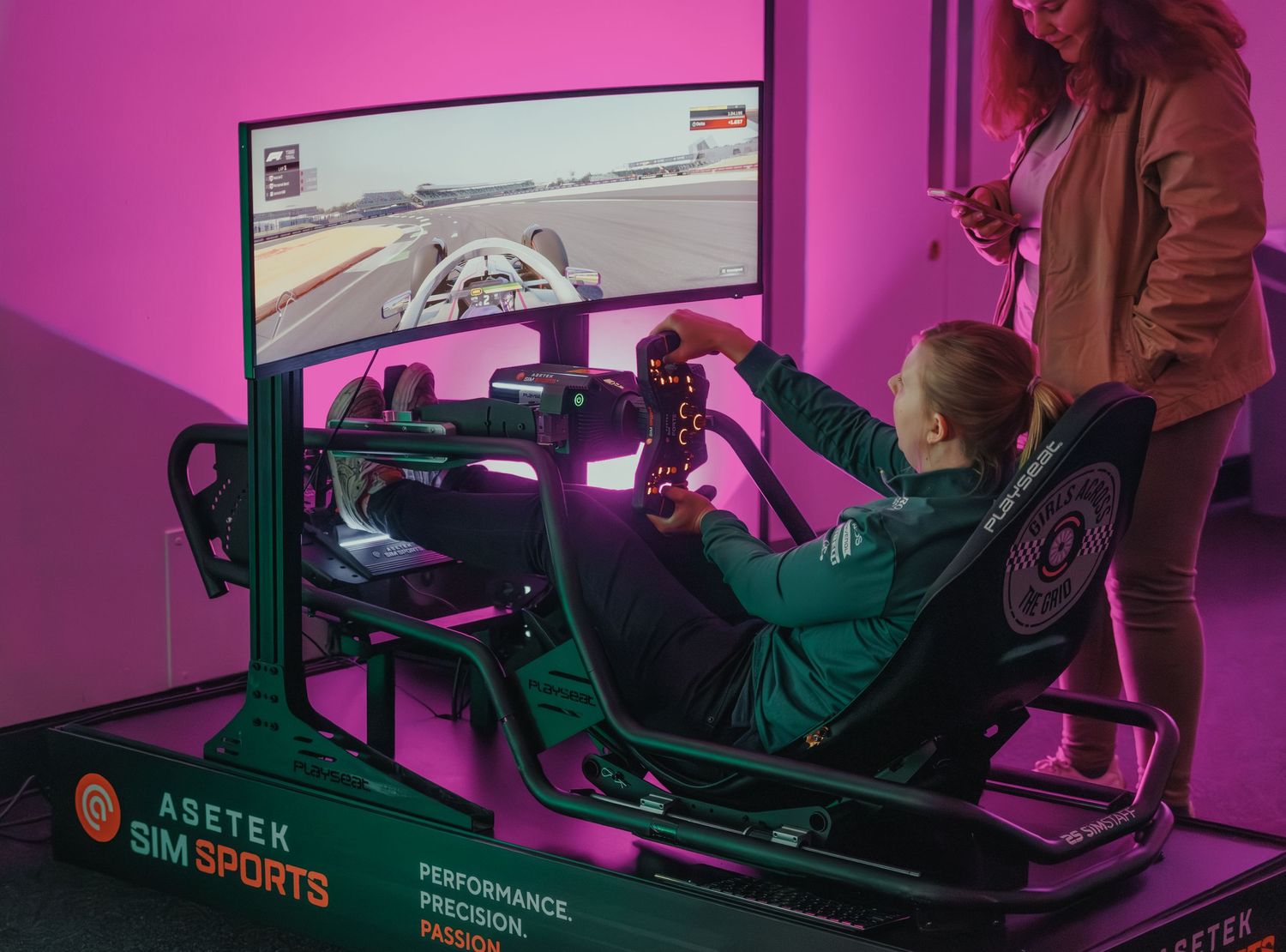 Person testing racing simulator with ultrawide screen in pink-lit gaming setup.