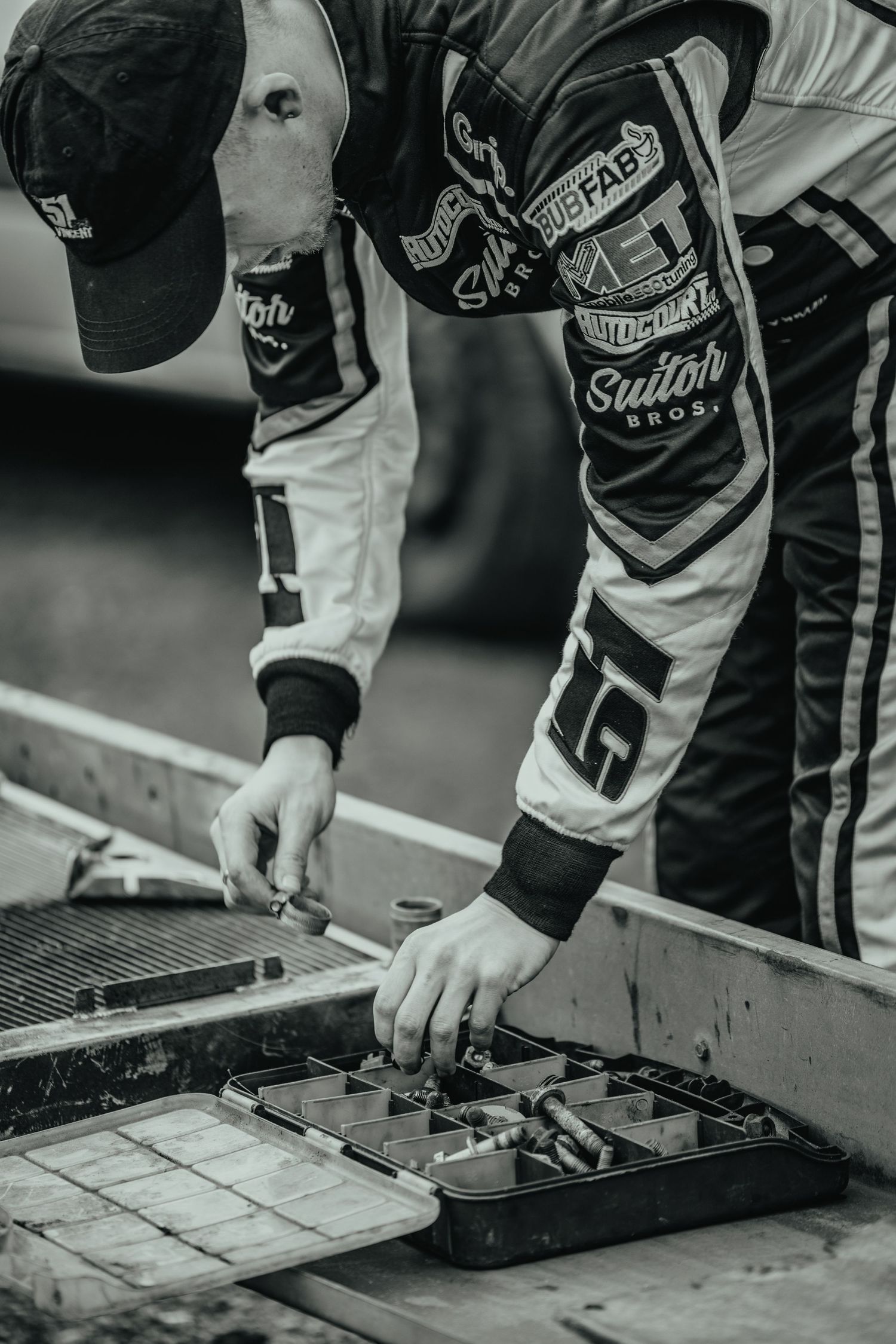 Black and white detail shot of racing suit and equipment during pit stop preparation.