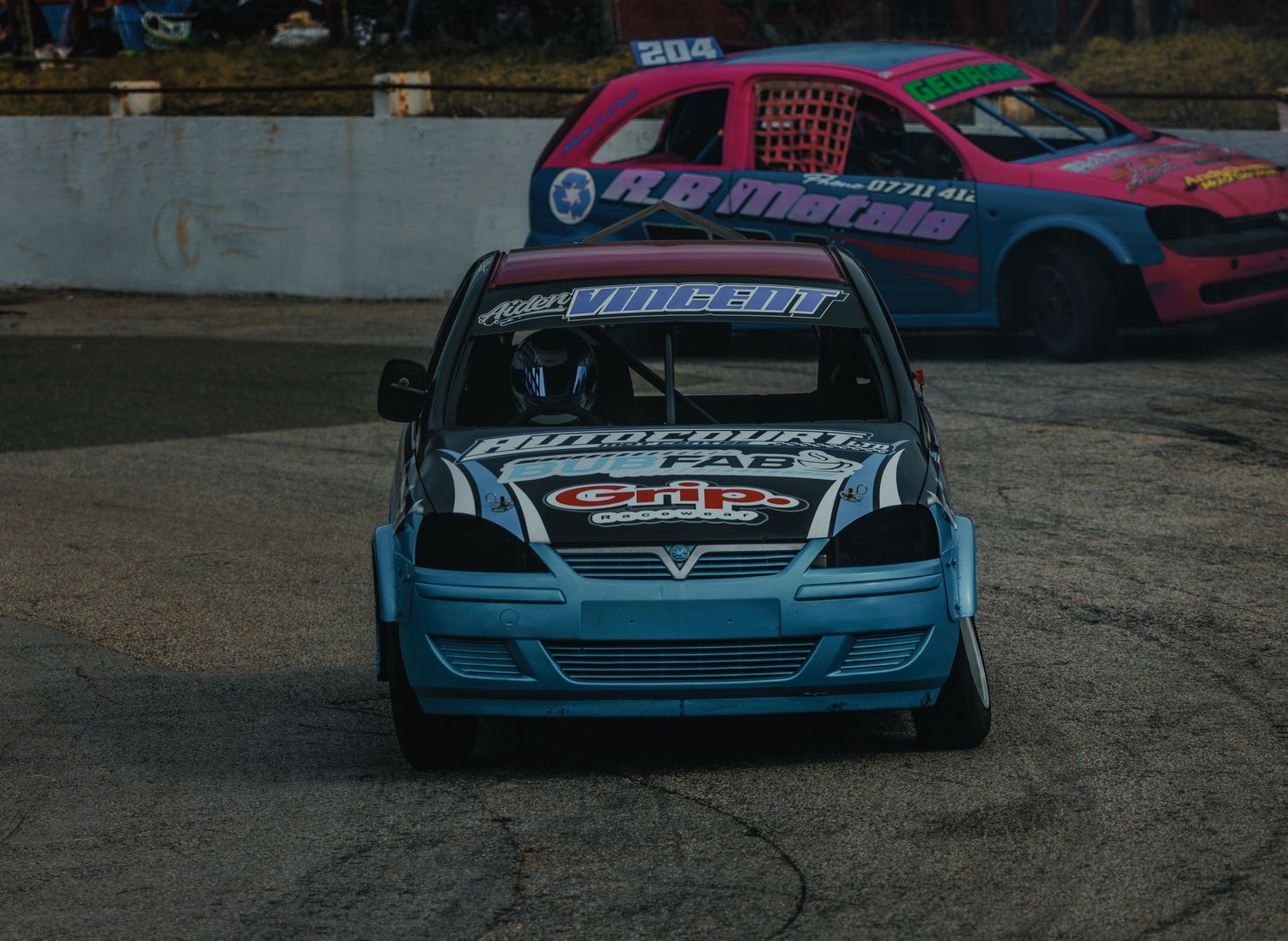 Two modified race cars, one blue and one pink, positioned on a racing track.