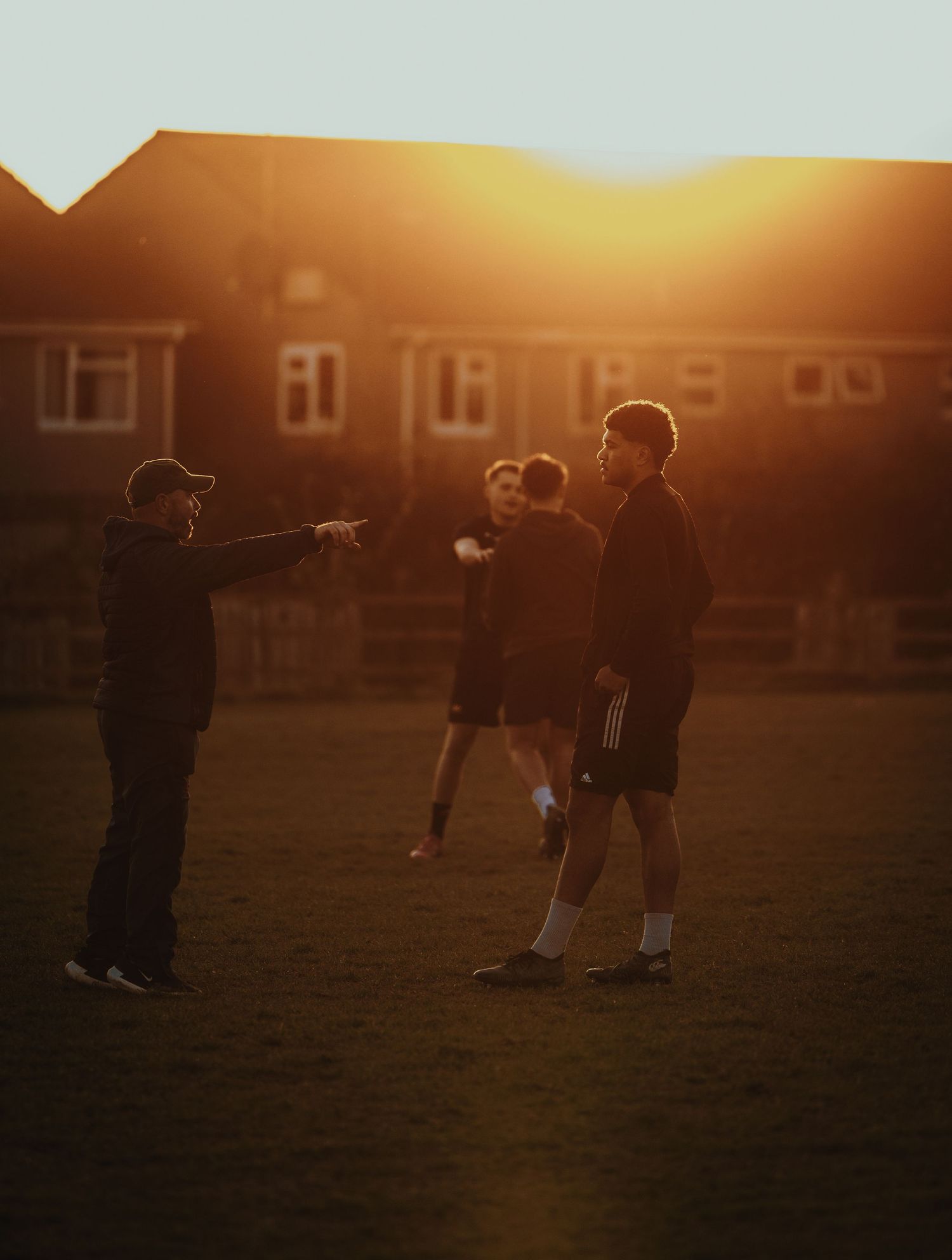 Silhouettes of rugby players discussing strategy during golden hour sunset.