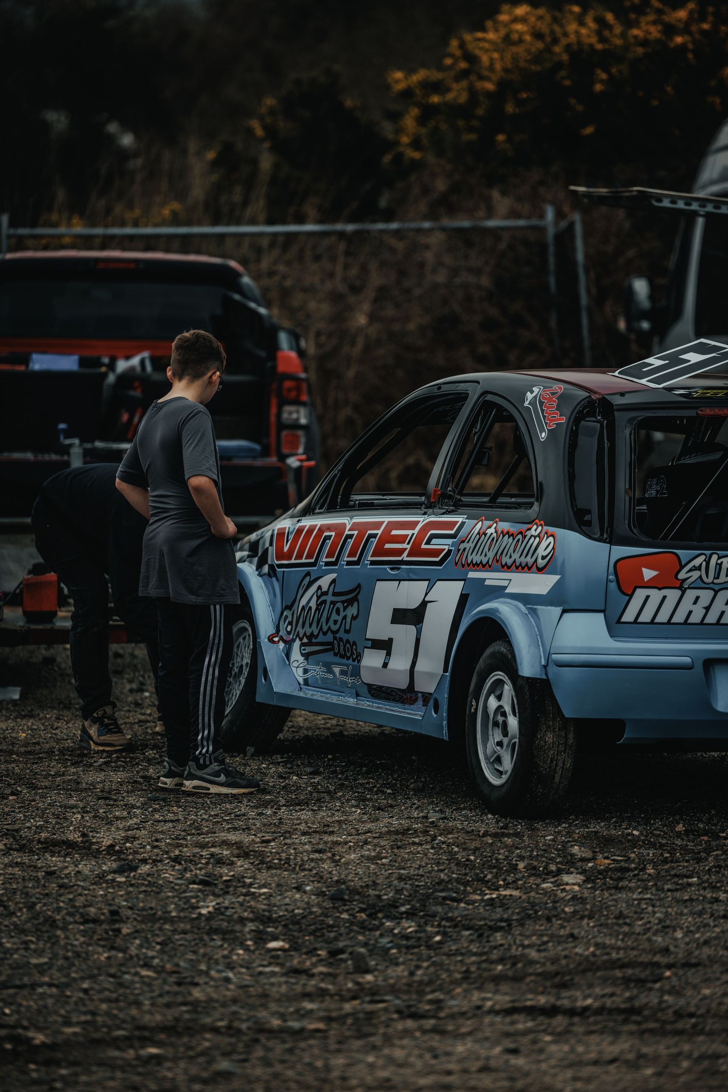 Light blue race car with number 51 and sponsor decals being examined in pit area.