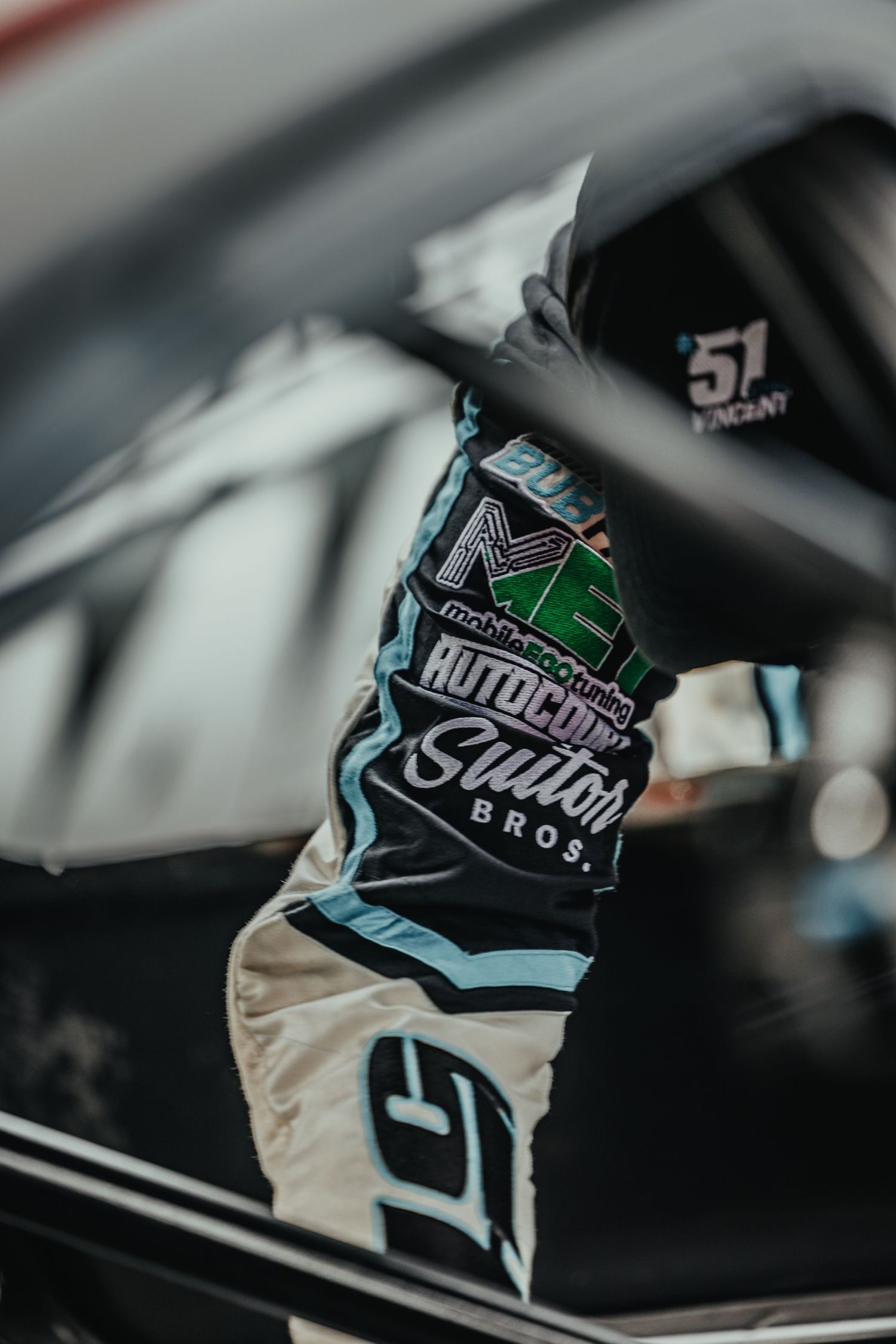 Racing suit detail showing Autocross sponsor logo and branding in teal and black.