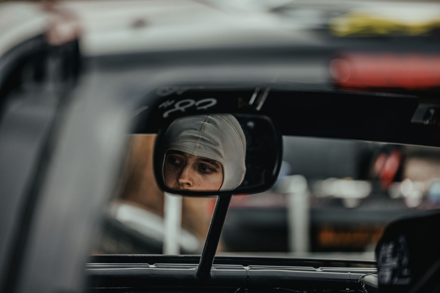 Racing driver reflection in side mirror of car showing focus through helmet visor during competition.