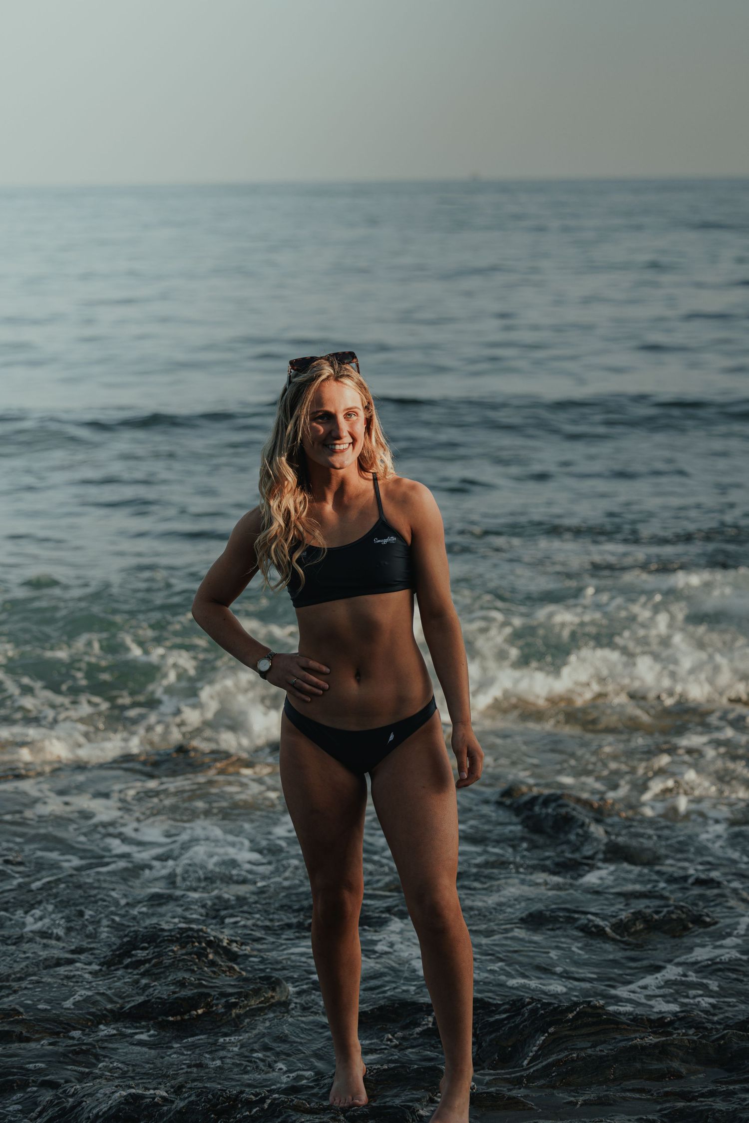 Athletic figure standing in ocean waves during golden hour beach photoshoot.