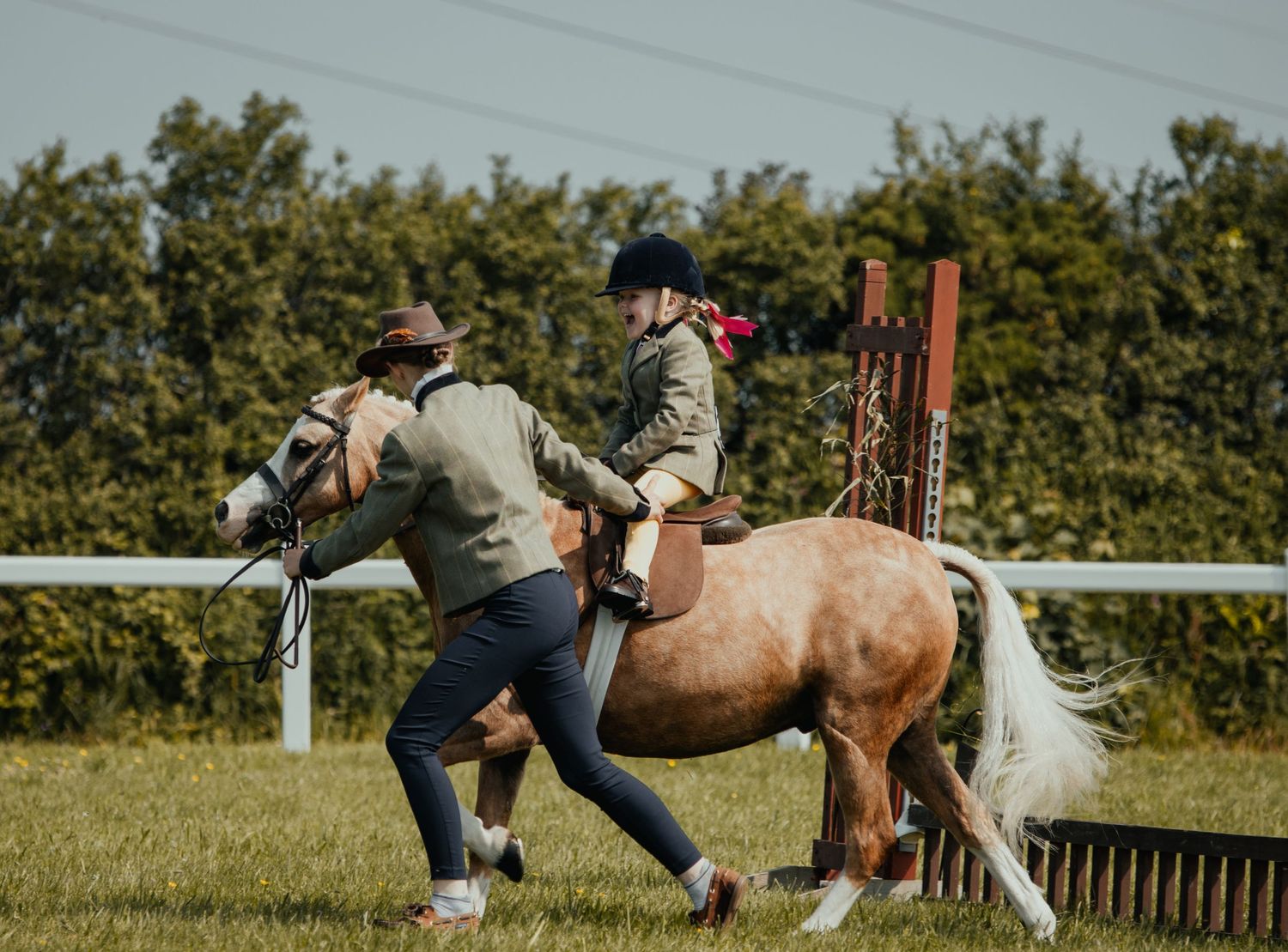 Handlers leading a palomino pony through a jumping exercise in an outdoor arena.