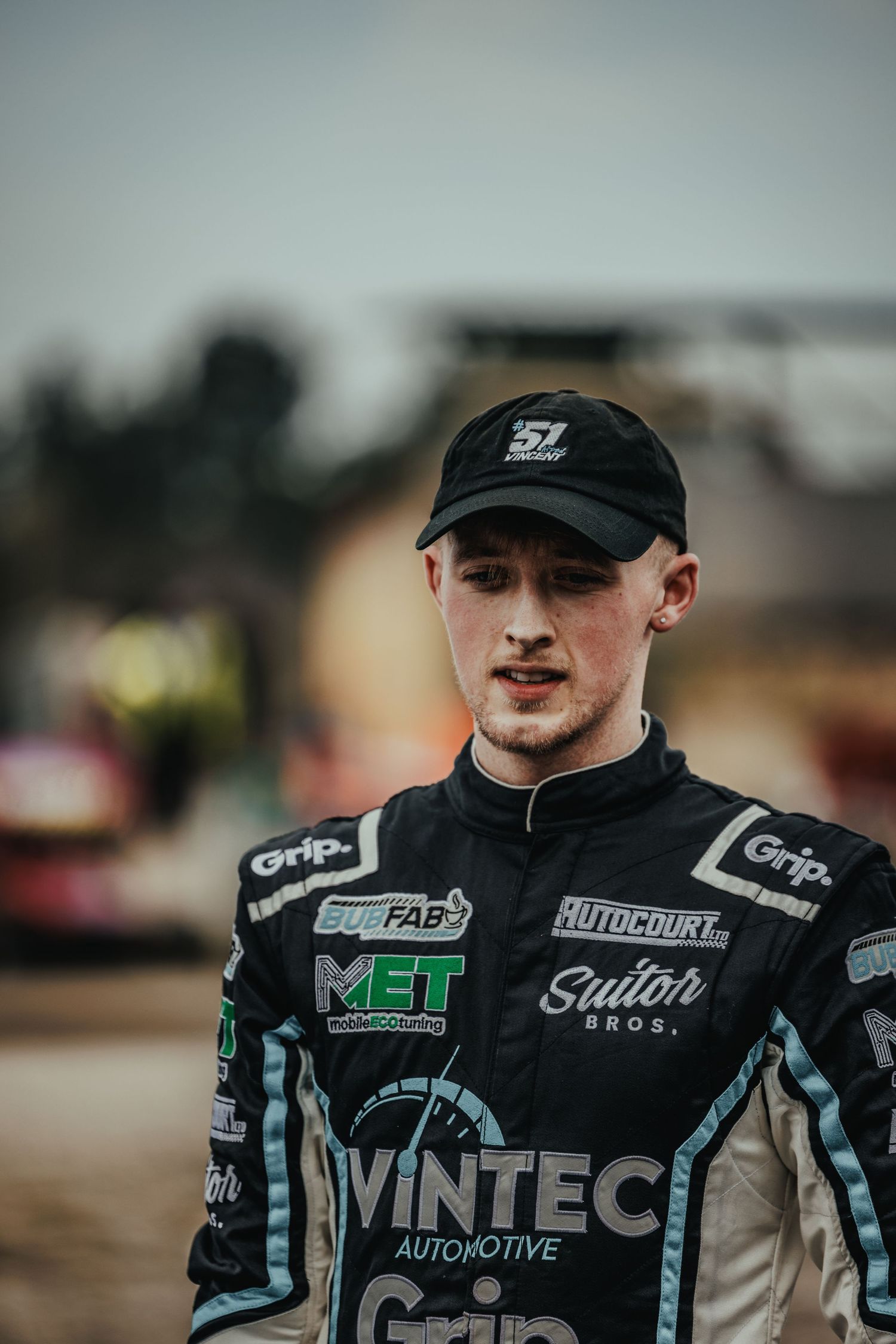 Close up of motorsport driver in Vintec racing suit and black cap.