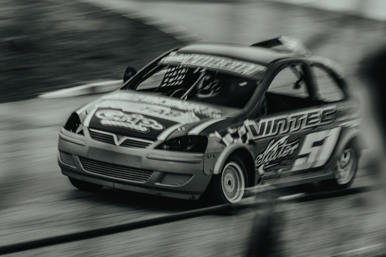Motion-blurred black and white photo of race car drifting during competition.