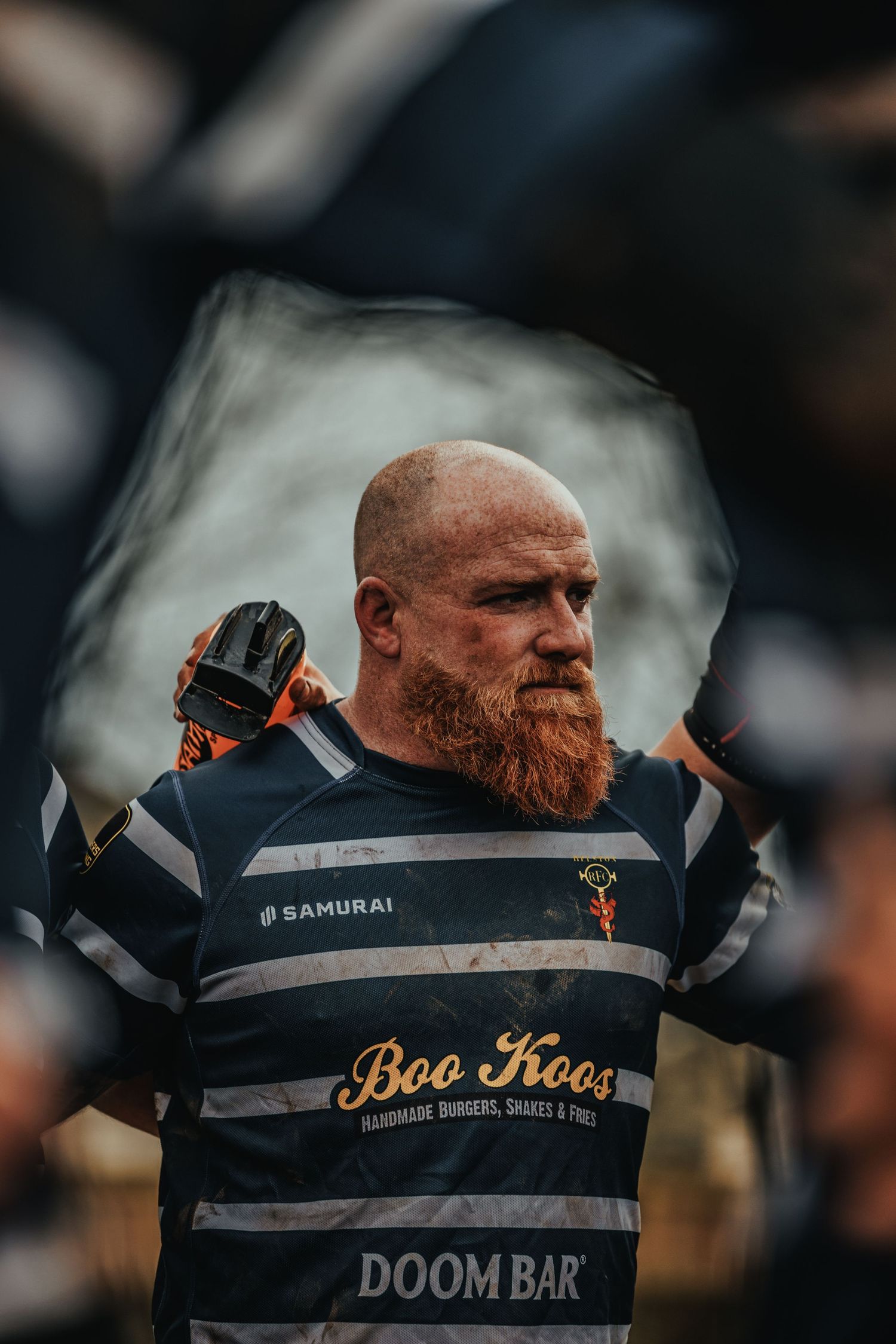 Rugby player wearing striped jersey with Boo Hoo and Doom Bar sponsorship on the field.