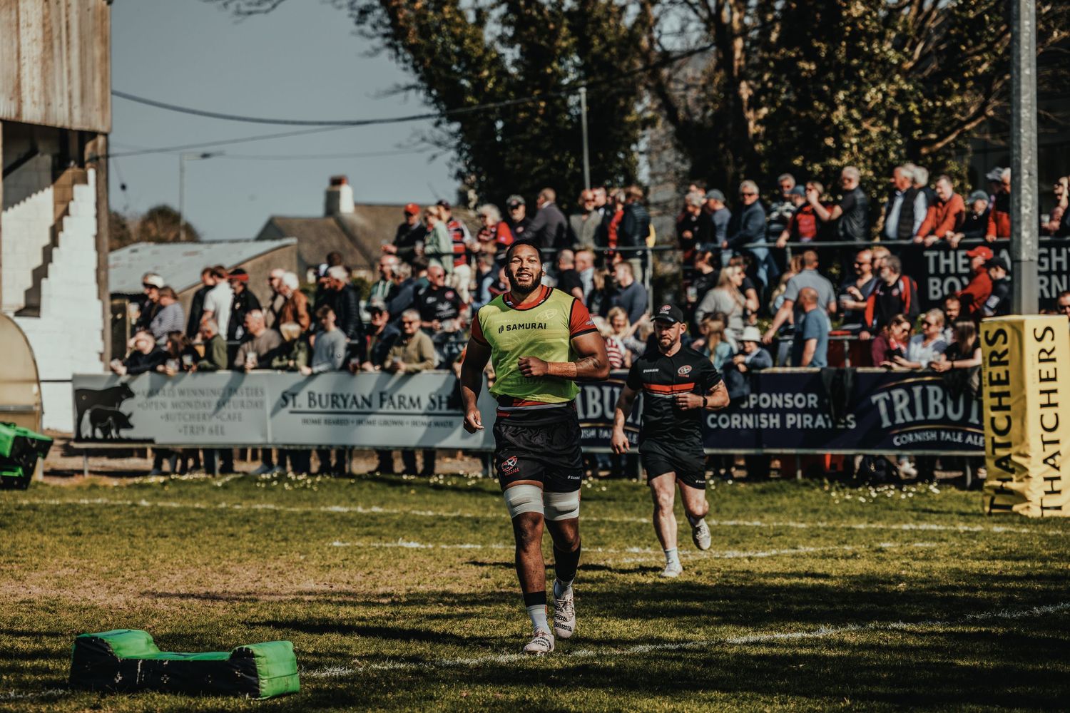 Rugby player in fluorescent vest performs on field with crowded stands in background.