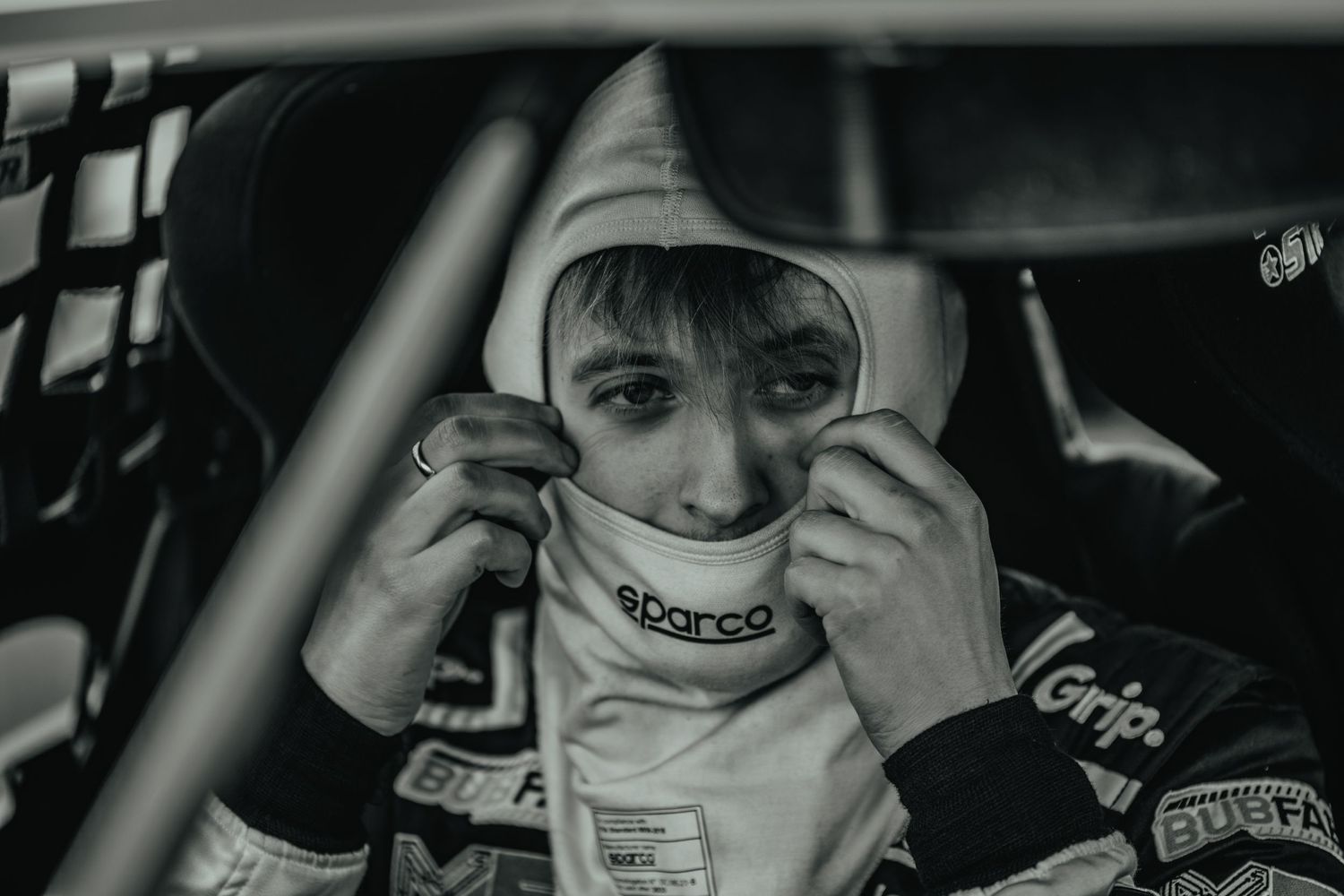 Race car driver adjusting helmet and safety equipment inside vehicle cockpit.
