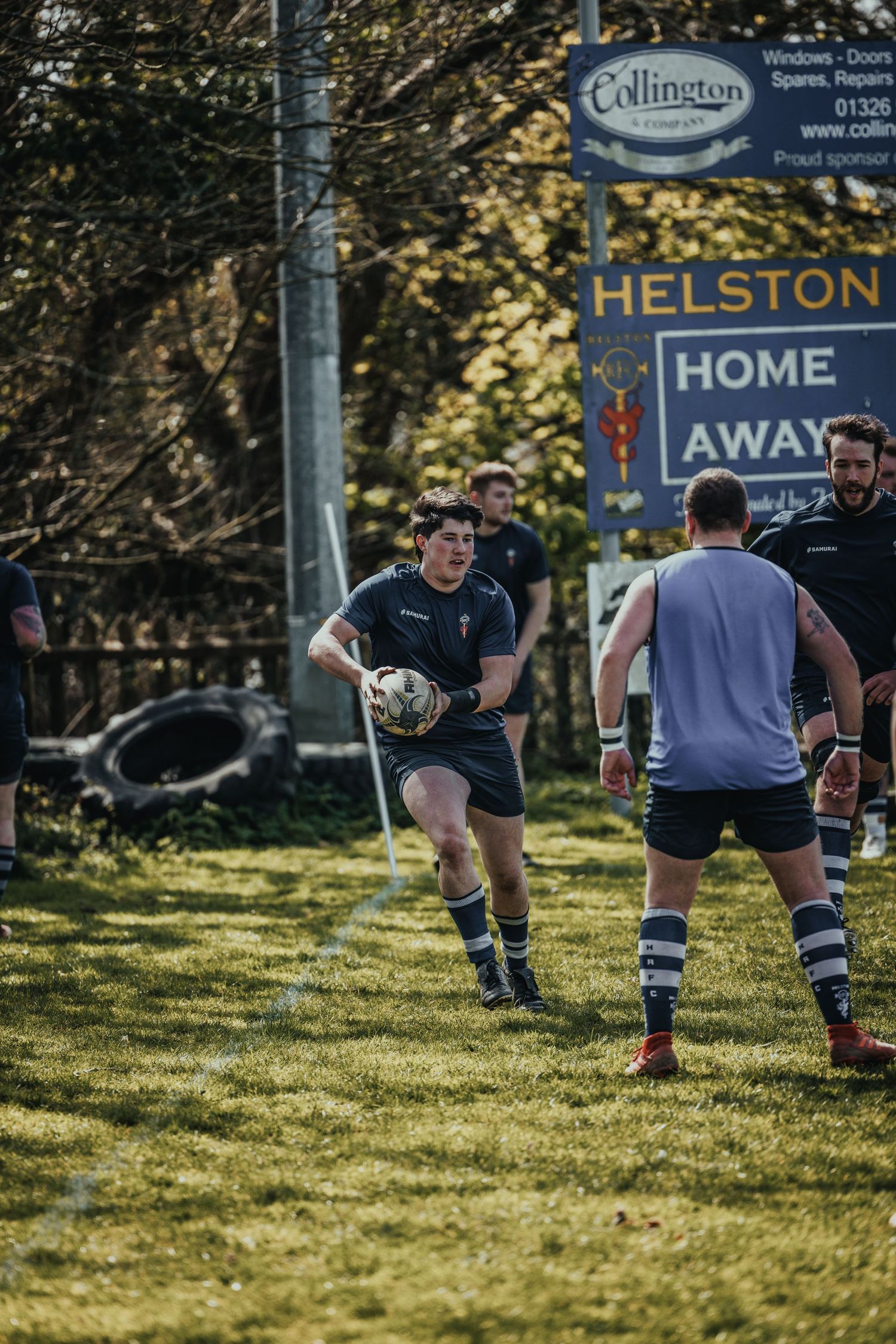 Rugby player carries ball during practice near Helston Home sign.