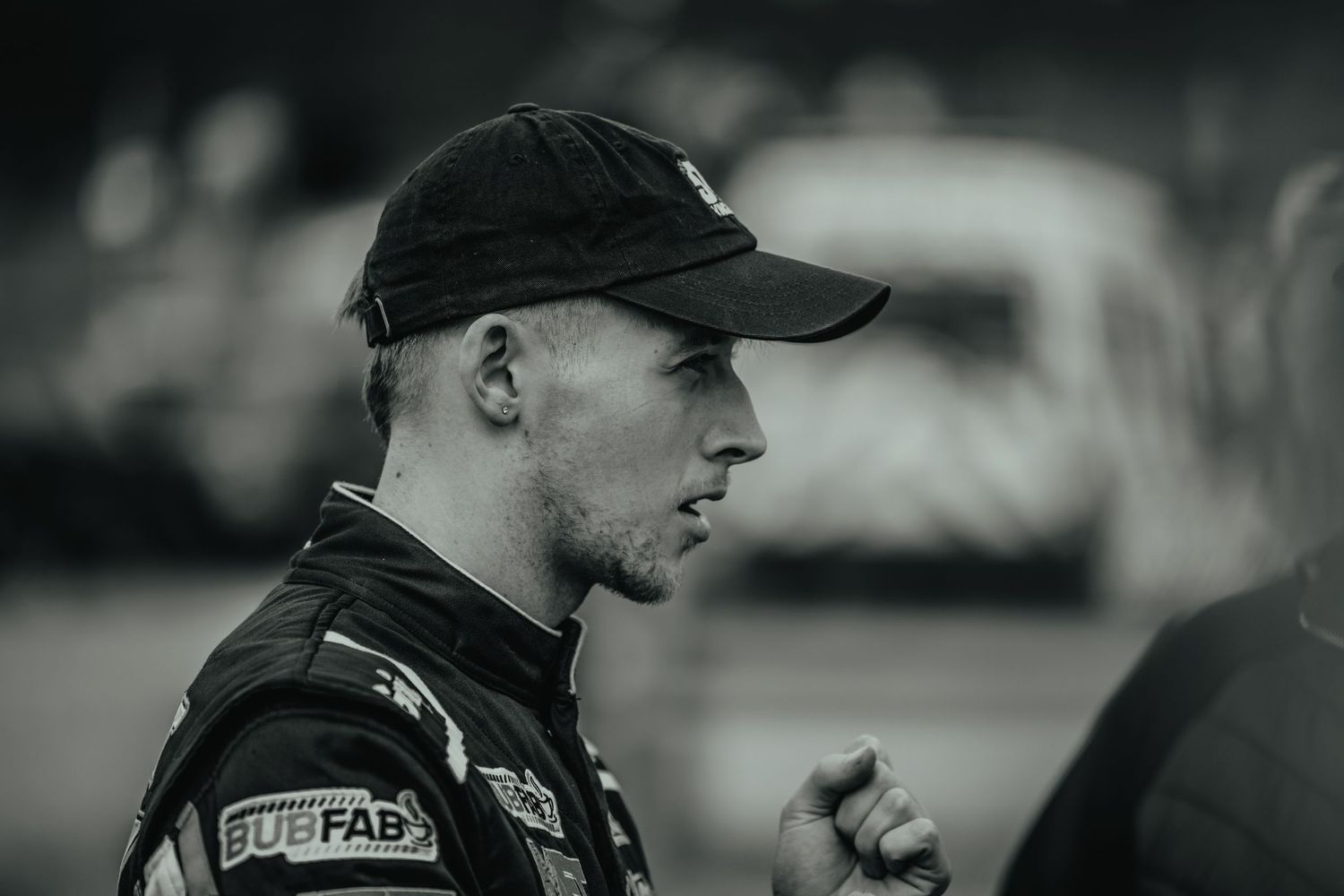 Side profile of racing competitor wearing black cap at outdoor motorsport event.