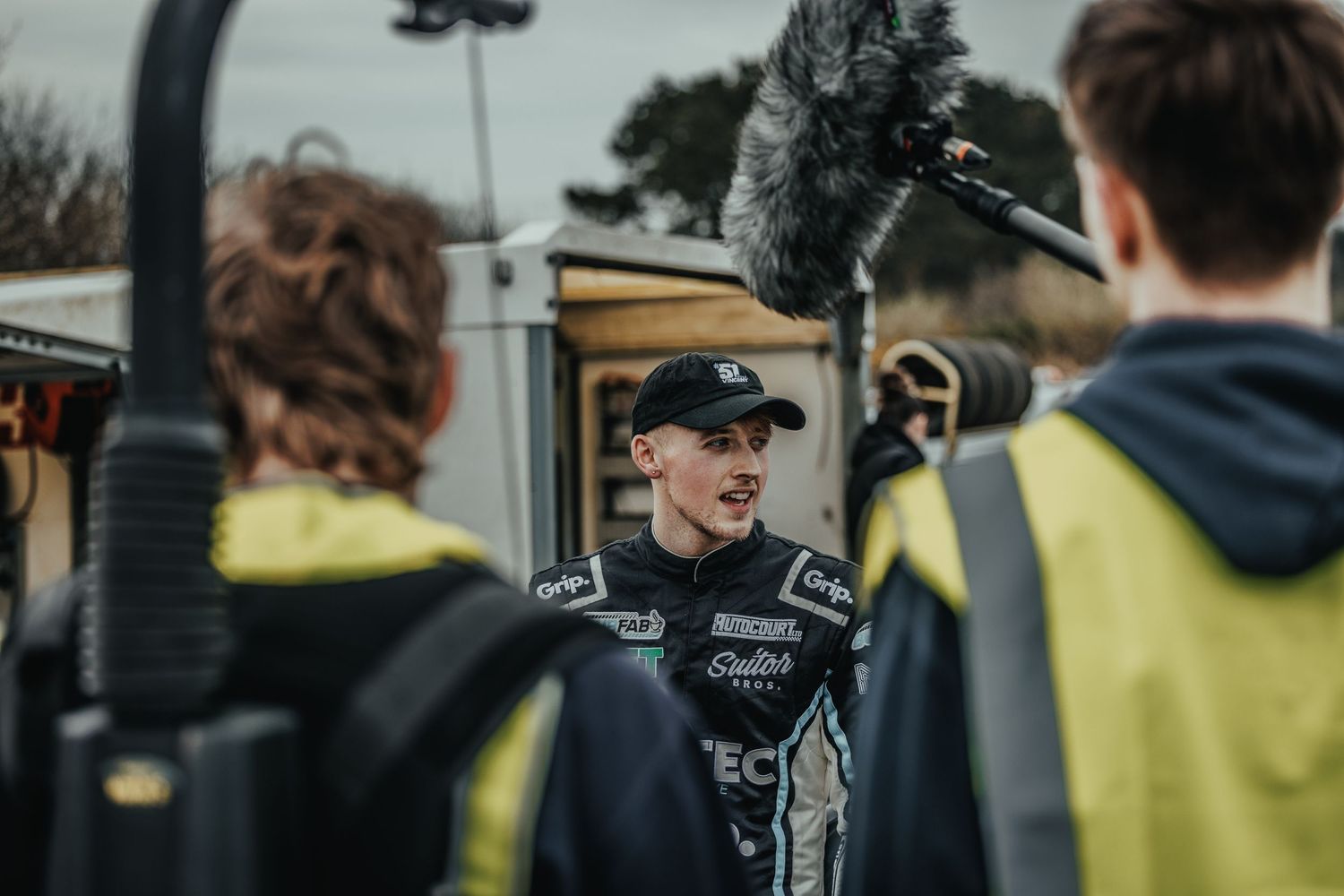 Racing driver being interviewed with microphone equipment at motorsport event.