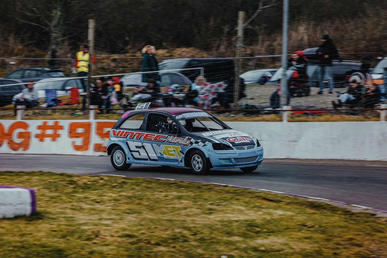 Race car speeds around track corner during competitive motorsport event.
