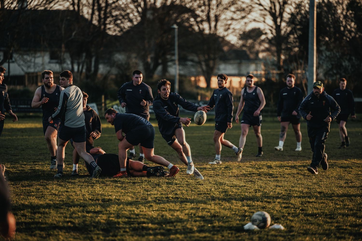Rugby players practicing drills on a grass field during sunset.