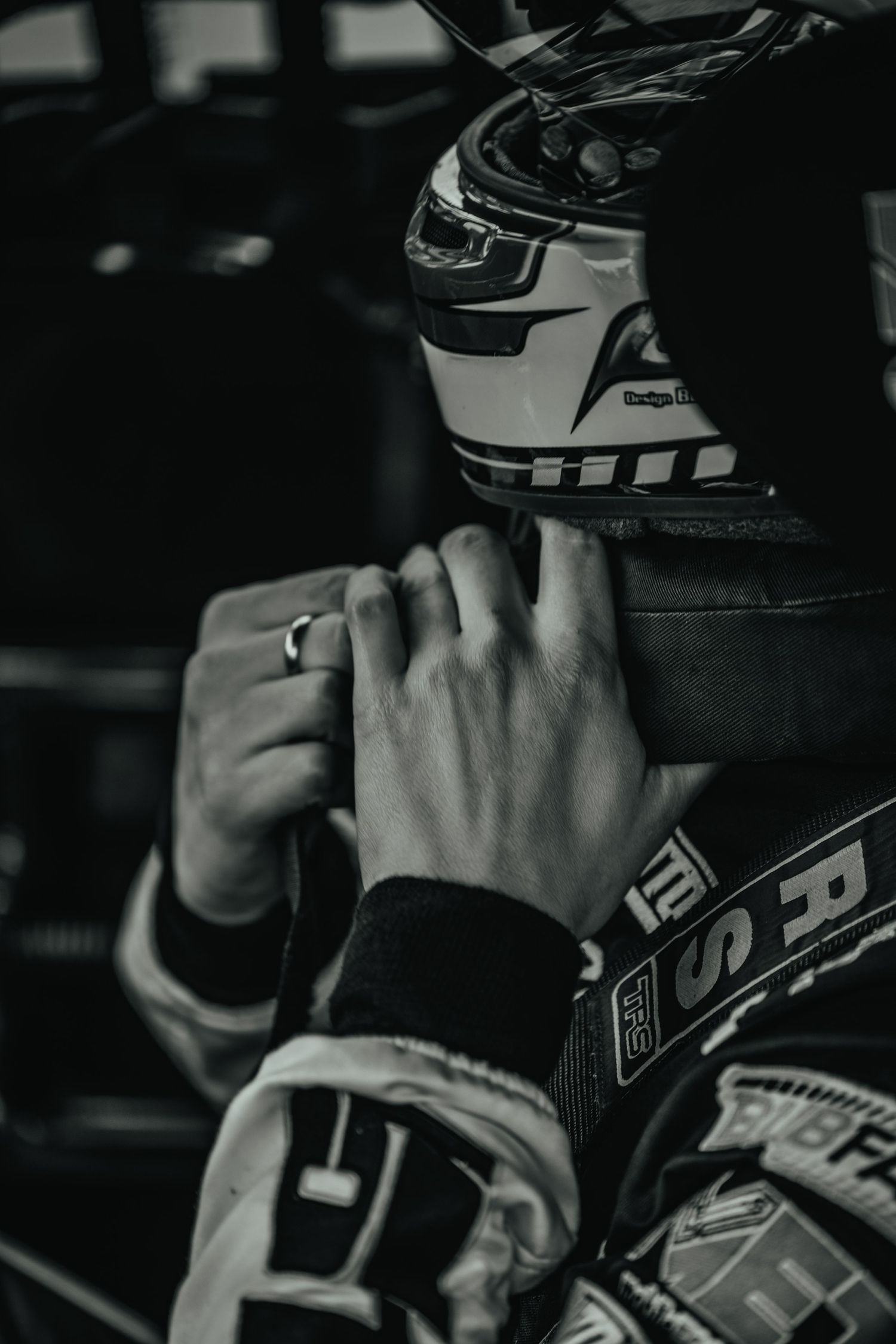 Close-up of hands adjusting racing helmet straps in black and white.