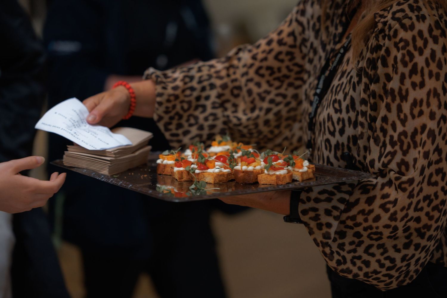 Woman in leopard print top serving bruschetta appetizers on a tray at a catered event.