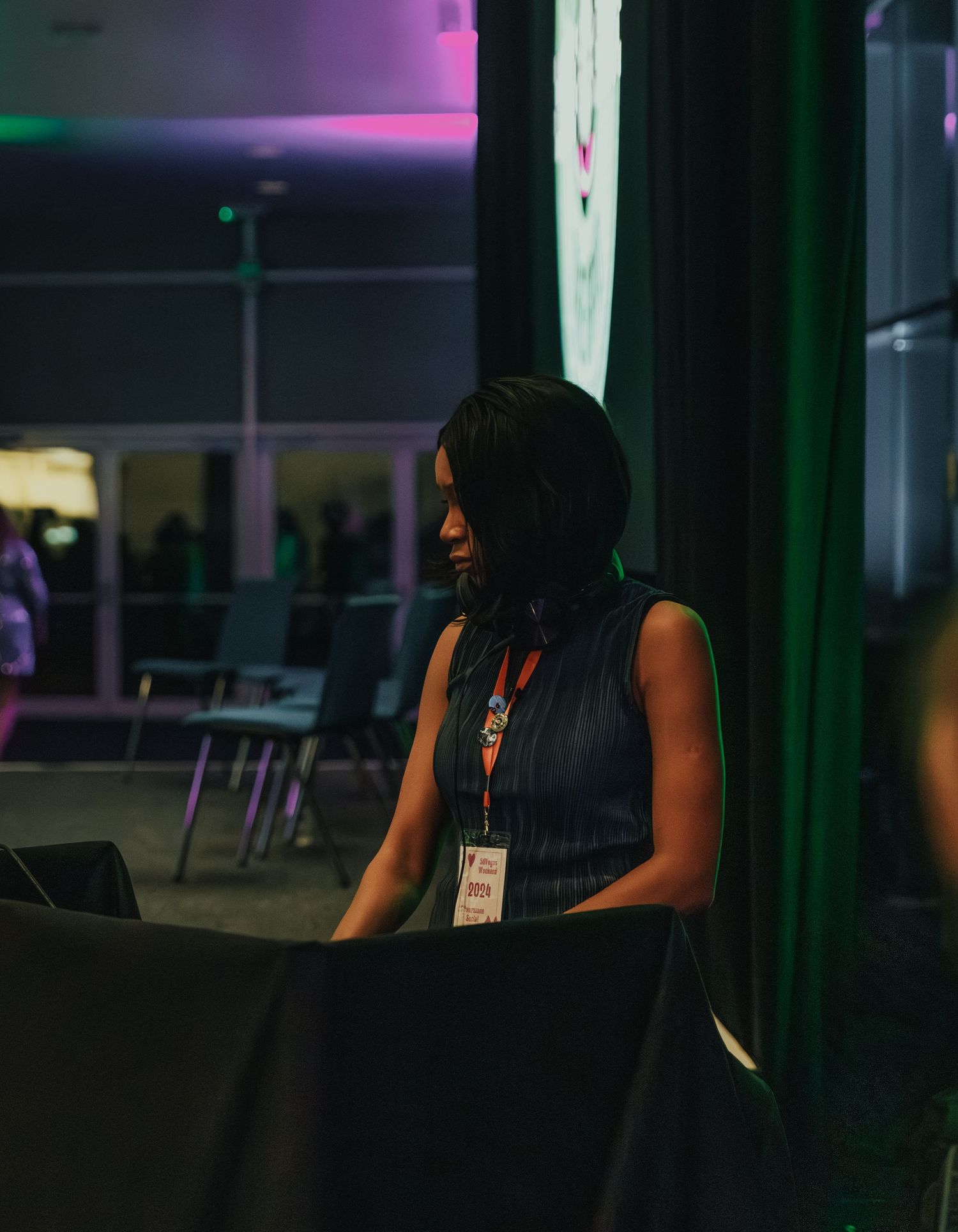 Person sitting in dimly lit venue with purple and green ambient lighting.