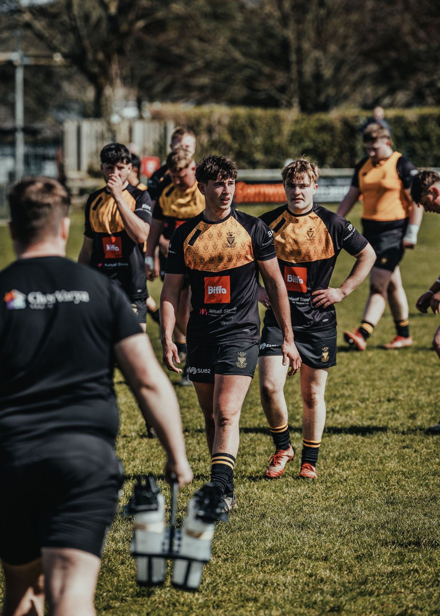 Rugby players in black and gold uniforms gather during practice session.