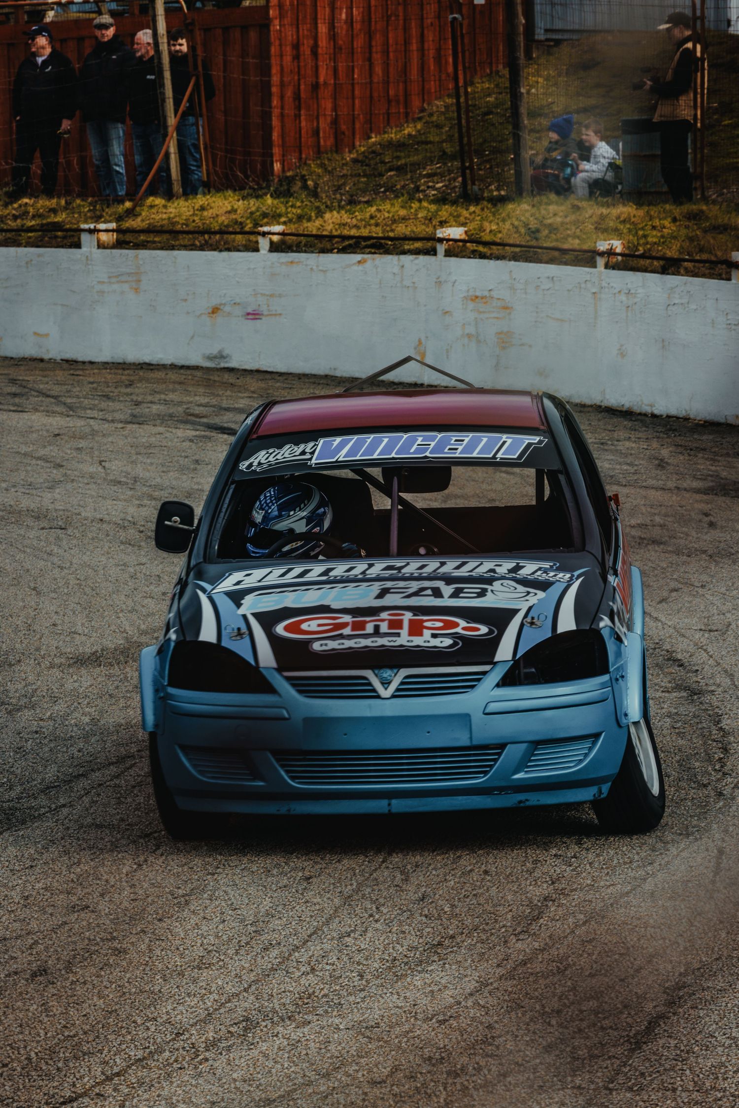 Blue race car with custom decals and modifications positioned on dirt track.