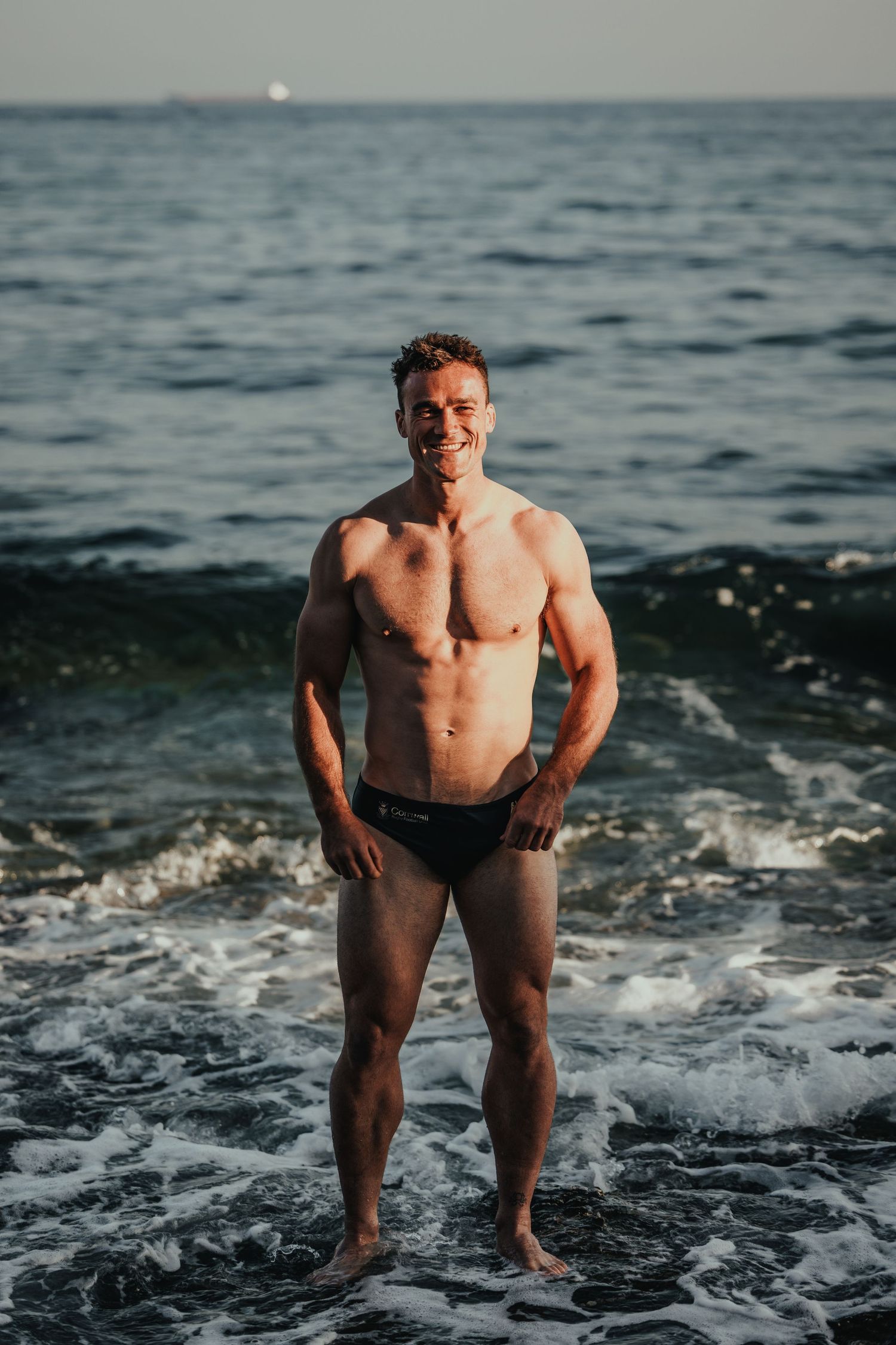 Athletic beach photoshoot with waves crashing in background at dusk.