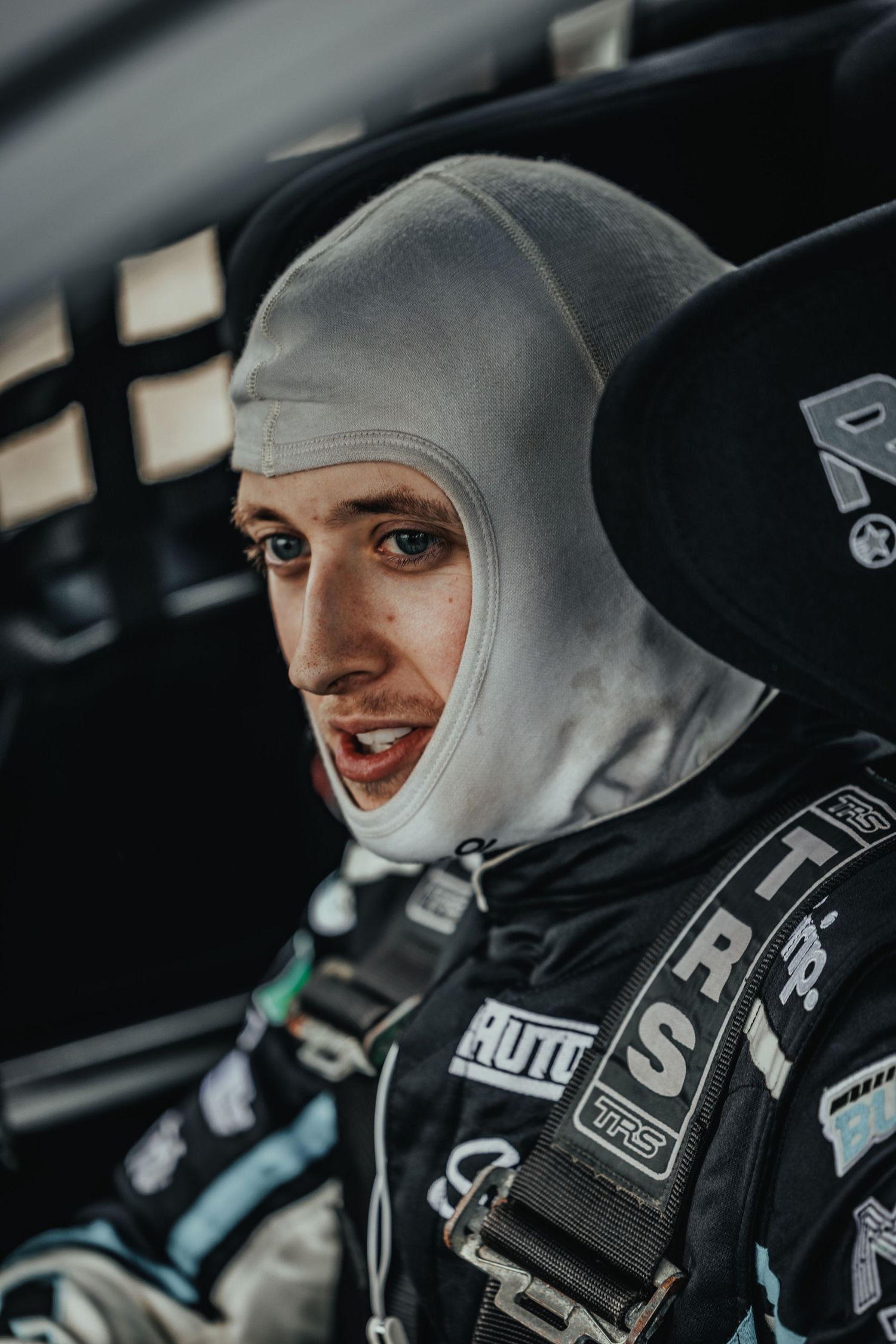 Race car driver wearing fireproof balaclava and safety equipment inside vehicle cockpit.