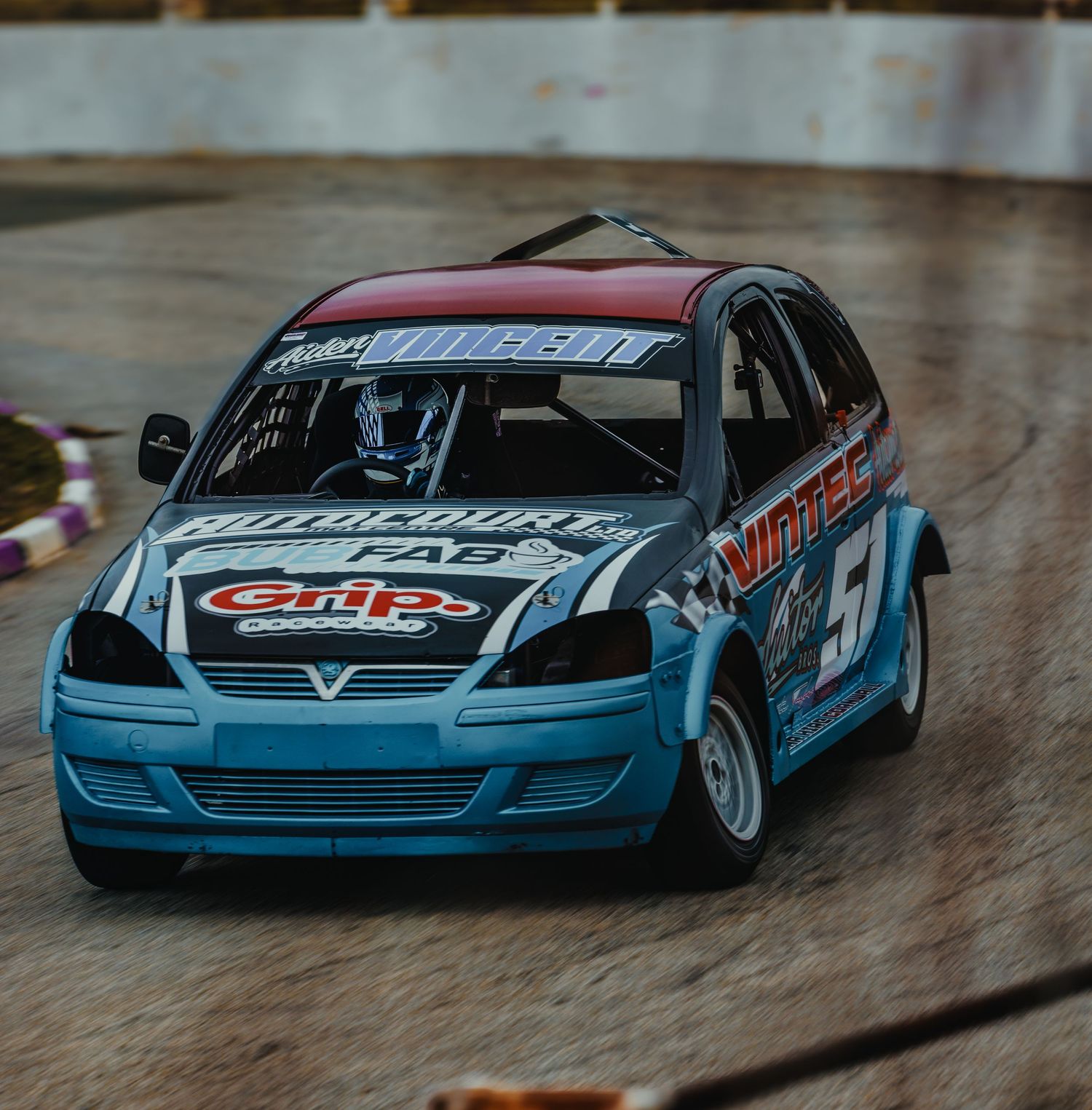 Blue racing car with sponsor decals photographed on indoor track surface.