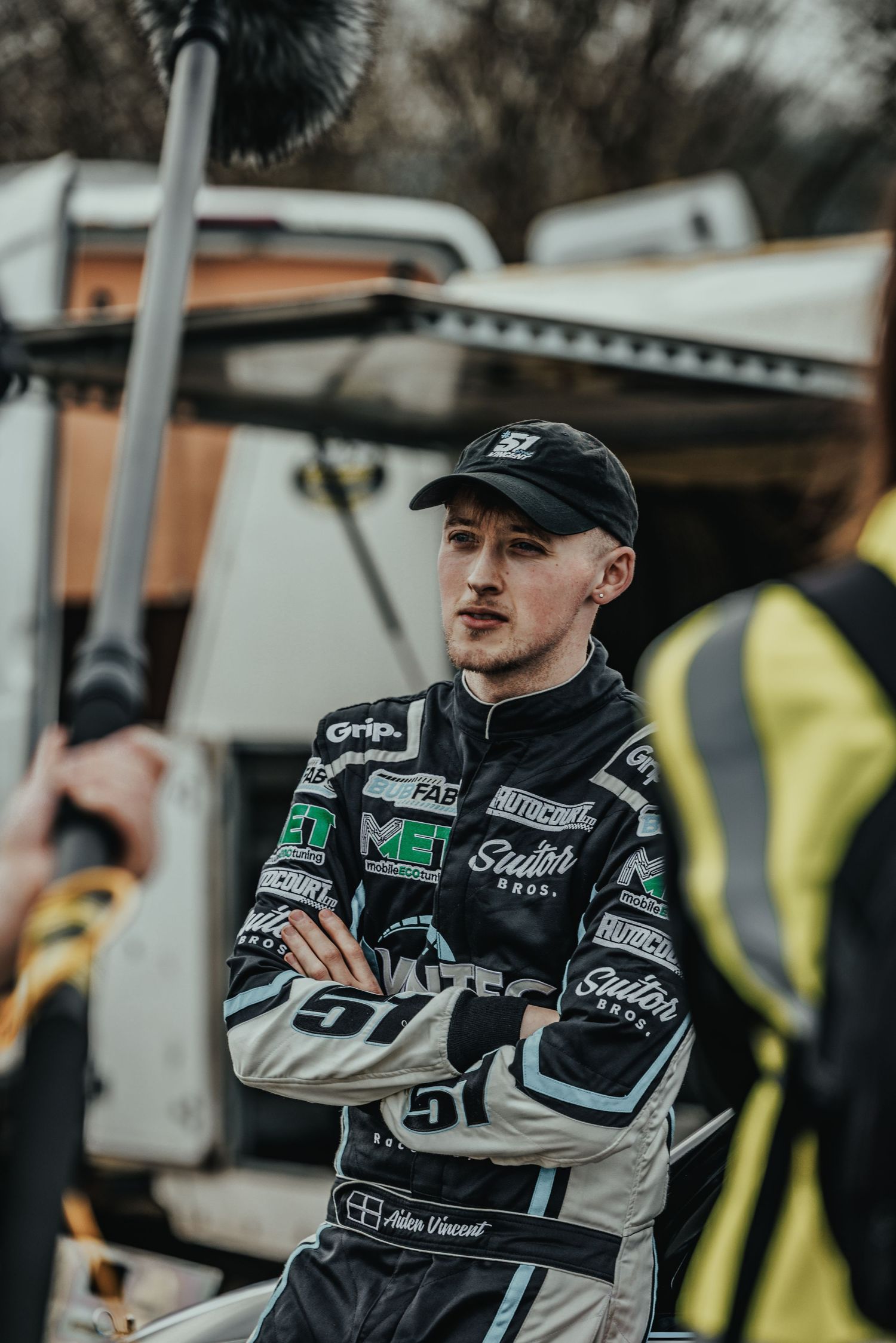 Professional racer in branded uniform standing near racing equipment.